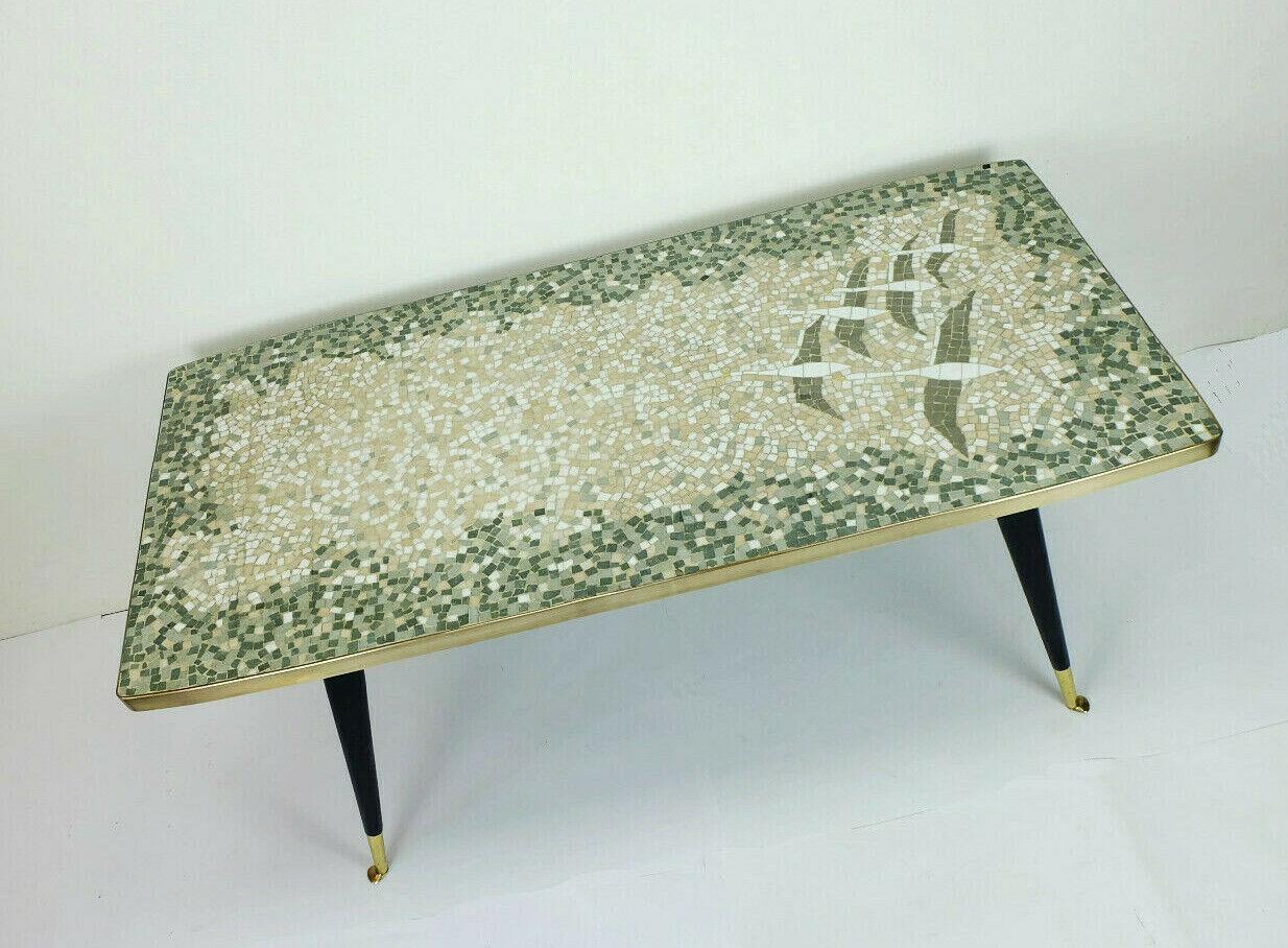 Very beautiful midcentury coffee table with mosaic top. Different shades of gray and greenish gray, white to beige in the middle, some yellow and black stones. The base is made of black lacquered solid wood, slanted legs with brass