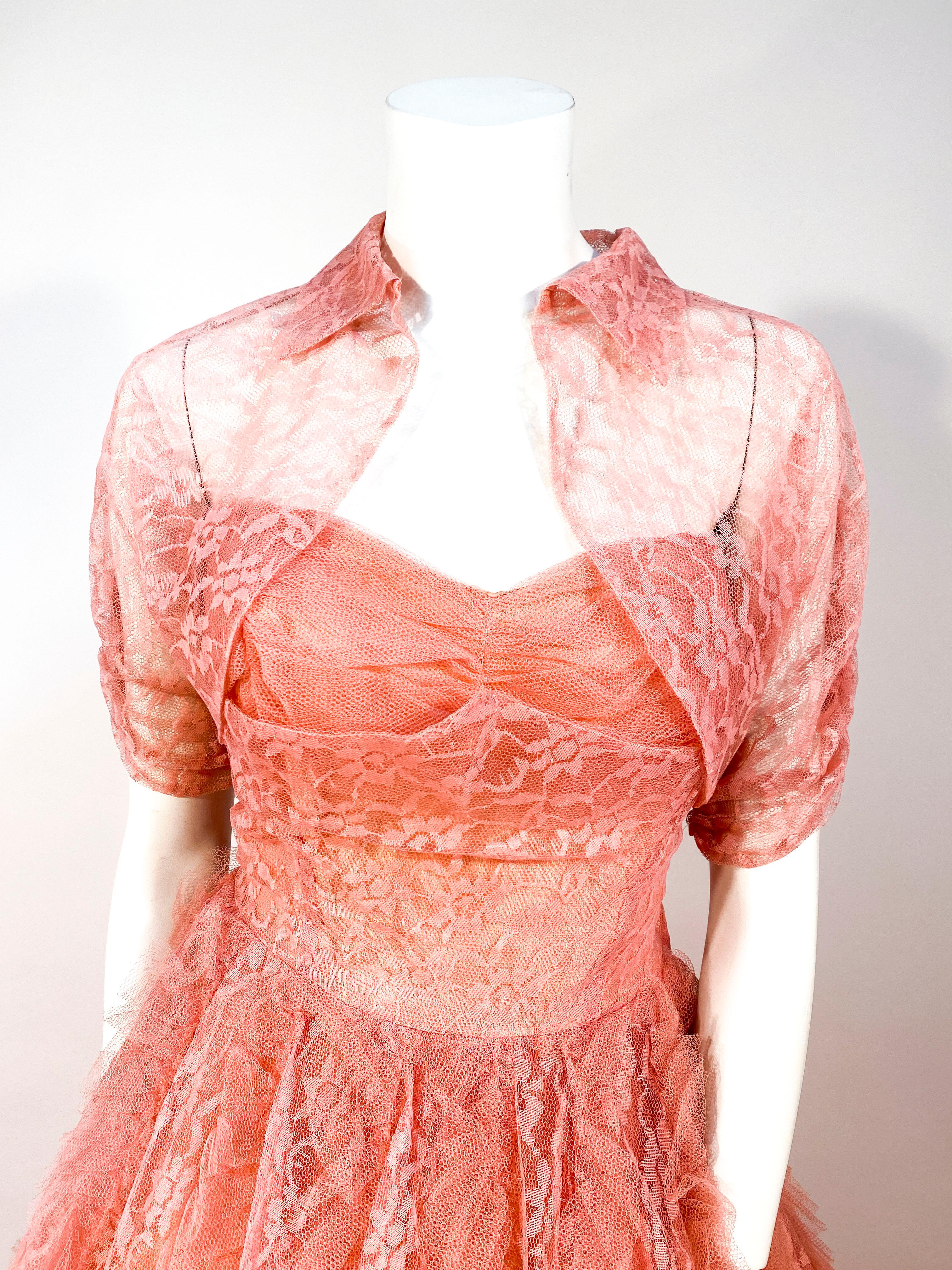 1950s coral lace and tulle evening dress or ball gown with matching bolero. The gown has a full-length skirt made of paneled lace and ruffles of tulle. The bodice is strapless with ruching over the bust. The bodice is entirely lined in satin and