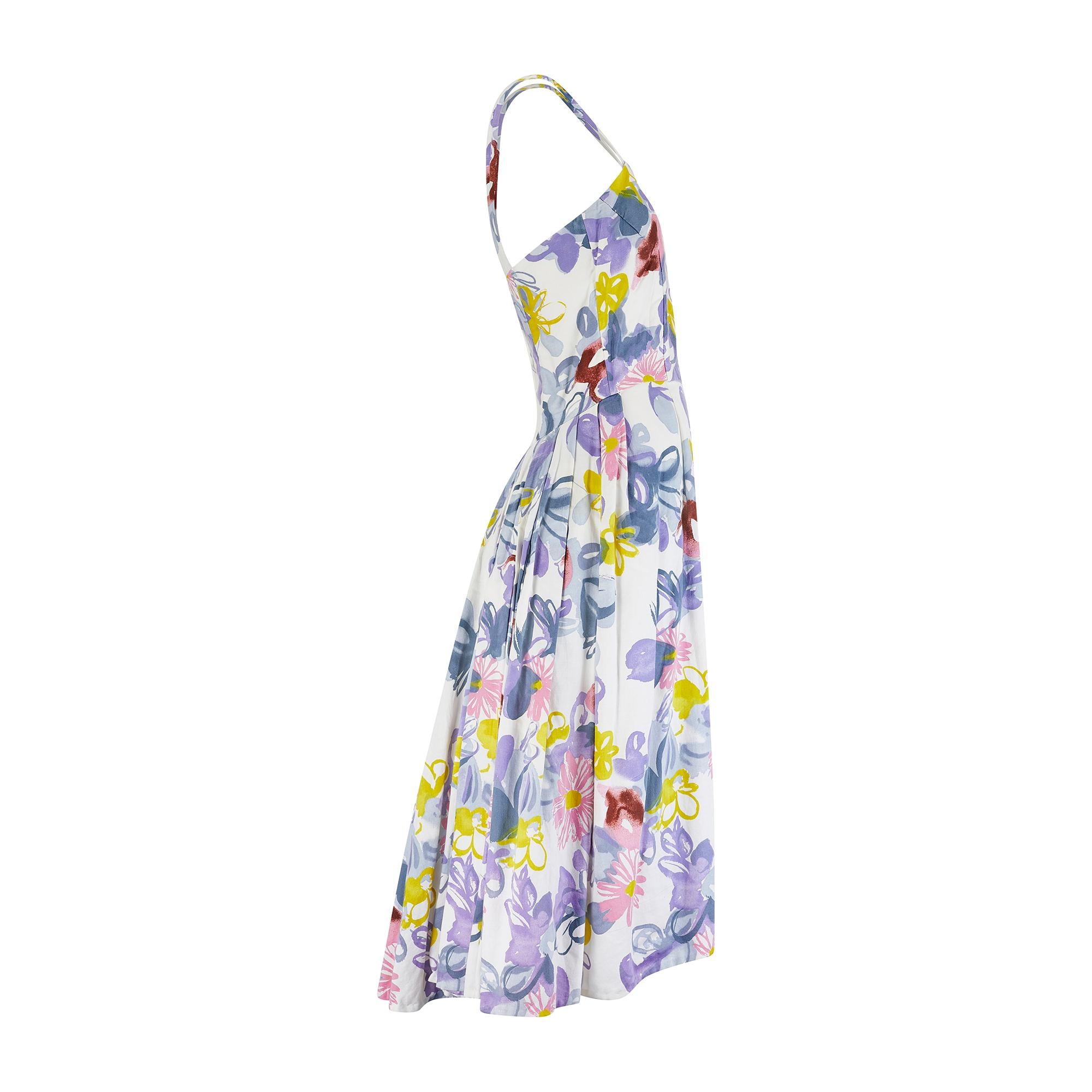 This lively sundress was made in the late 1950s to early 1960s and features some unusual design details. Tailored from soft cotton, it is patterned with vivacious abstract florals in shades of grey-blue, chartreuse and smudgy pink and burgundy. The