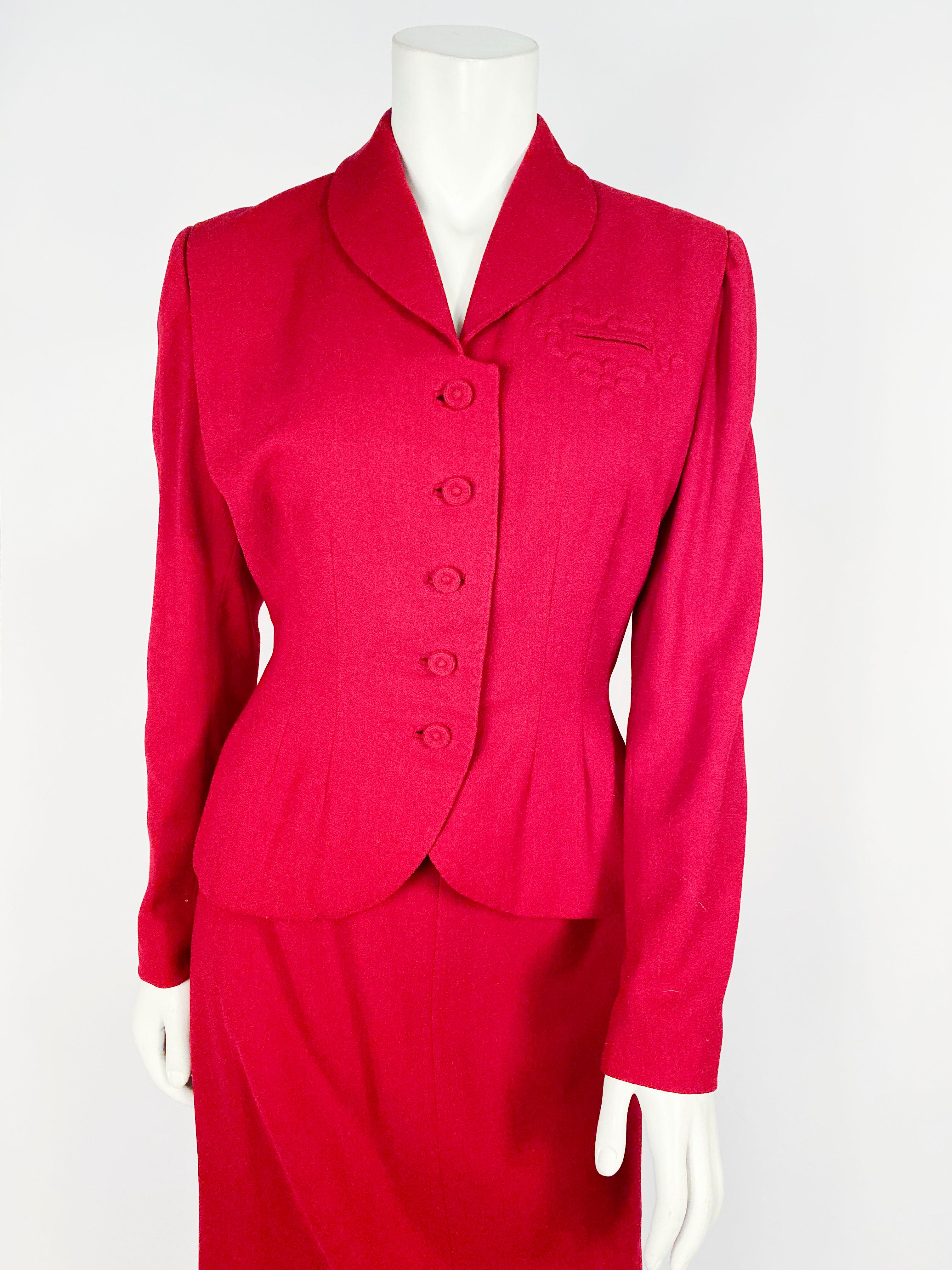 1950s cranberry red wool crepe suit with trapunto embroidery around the faux pocket on the face of the suit jacket finished with a hand-covered button, and lining/top stitch all hand-sewn. 