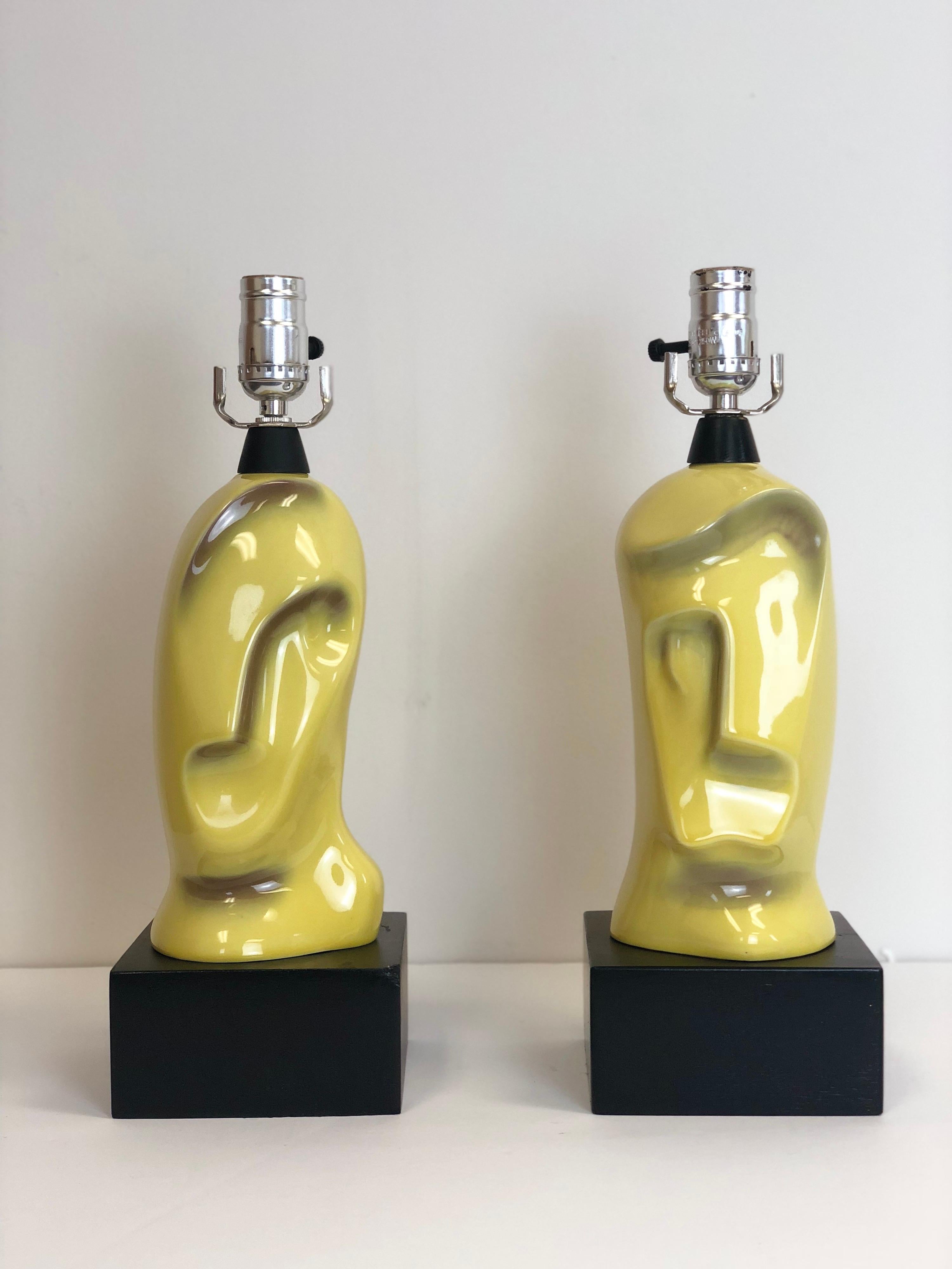 We are very pleased to offer a pair of abstract, ceramic face table lamps by Yasha Heifetz, circa the 1950s. One lamp showcases a woman and the other the face of a man. These modernist table lamps are glazed in a light green. New 14” drum shades in