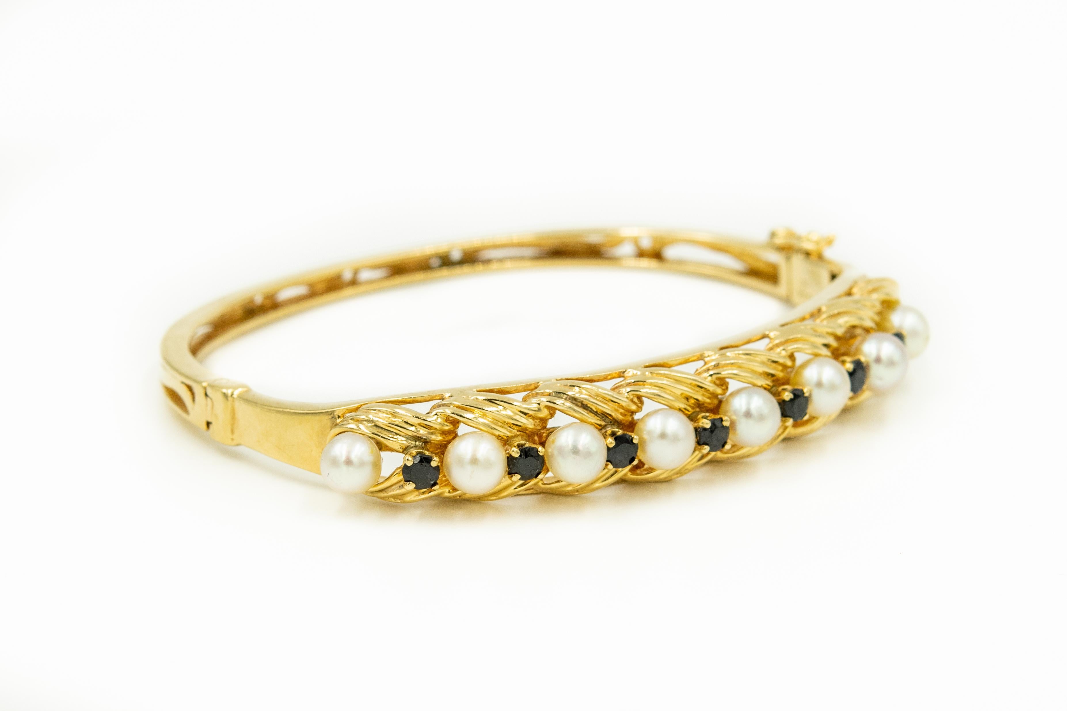 Classic 1950s elegant cultured pearl bangle featuring 8 cultured pearls (approximately 4.75 mm each) accented with prong set faceted sapphires in a 14k yellow gold bangle with a simple shiny finish the sides.  The back is pierced.  The bracelet