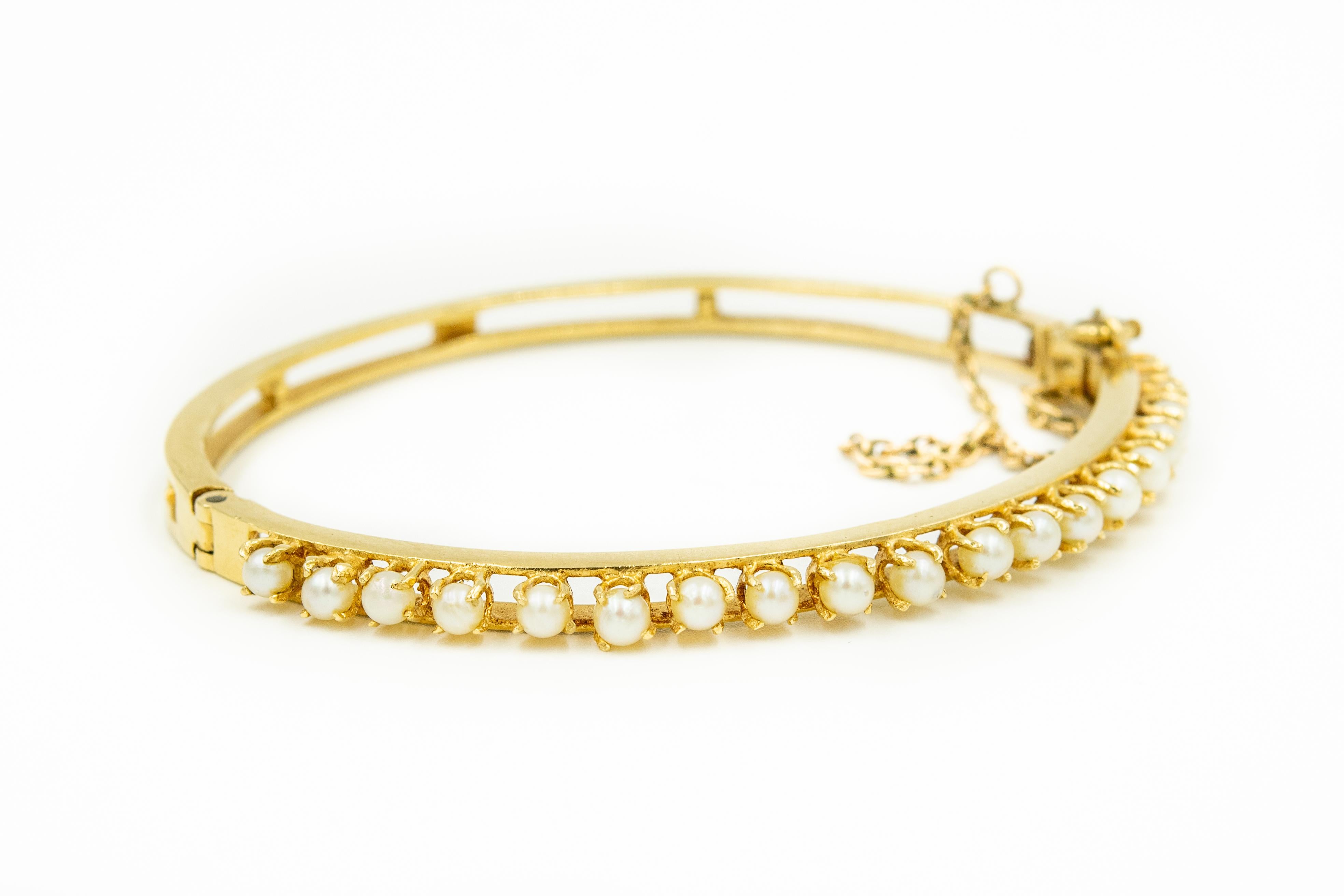 Classic 1950s elegant cultured pearl bangle featuring 19 prong set cultured pearls (approximately 3.3 mm each) set in a 14k yellow gold bangle with a simple shiny finish the sides.  The back is open.  The bracelet hinges open and closes with a push