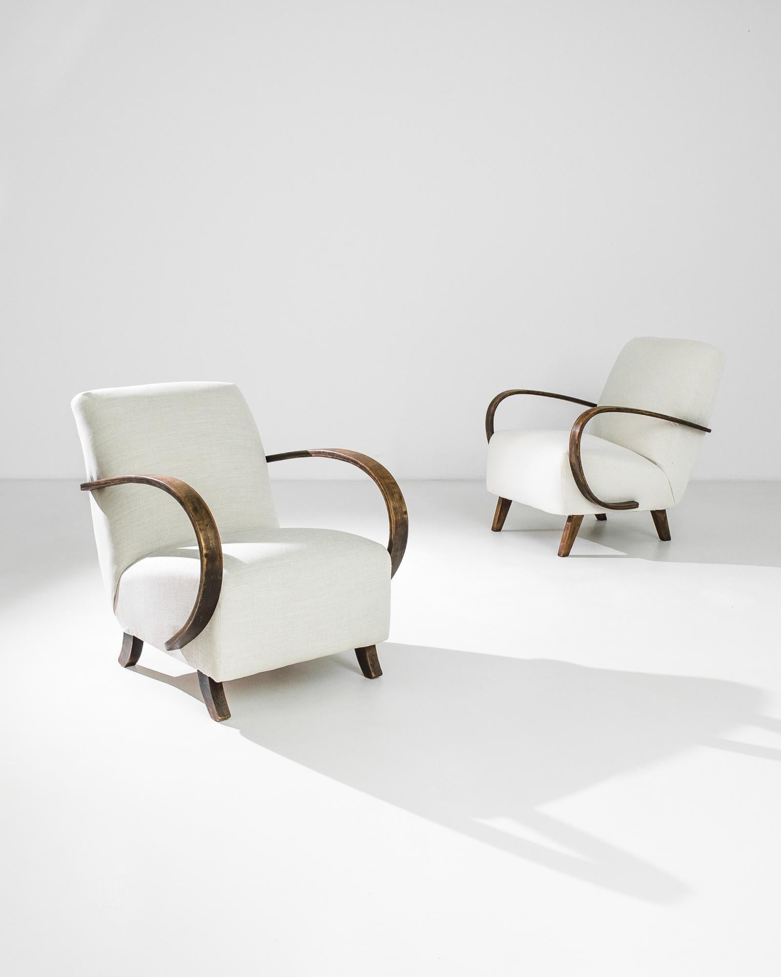 A pair of armchairs by Czech furniture designer J. Halabala. Made in the 1950s, the eye-catching Silhouette and comfortable design has an enduring appeal. A deep upholstered seat upon curved wooden feet is framed by the dramatic curves of the