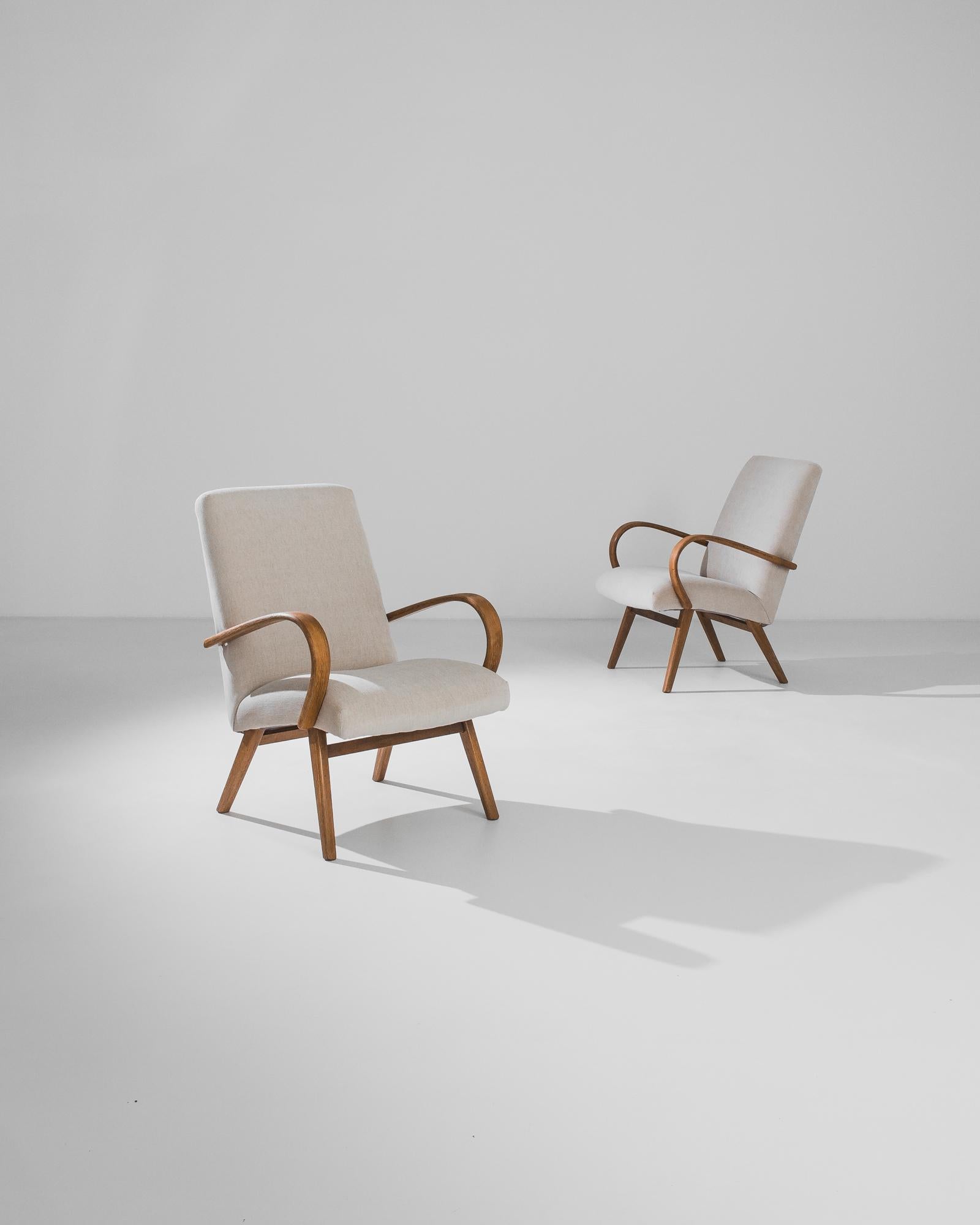 Fabriquée dans l'ancienne Tchécoslovaquie par le designer de meubles J. Halabala, cette paire de fauteuils en bois courbé des années 1950 a été retapissée dans un tissu neutre actualisé. La courbe audacieuse des accoudoirs et l'angle des pieds