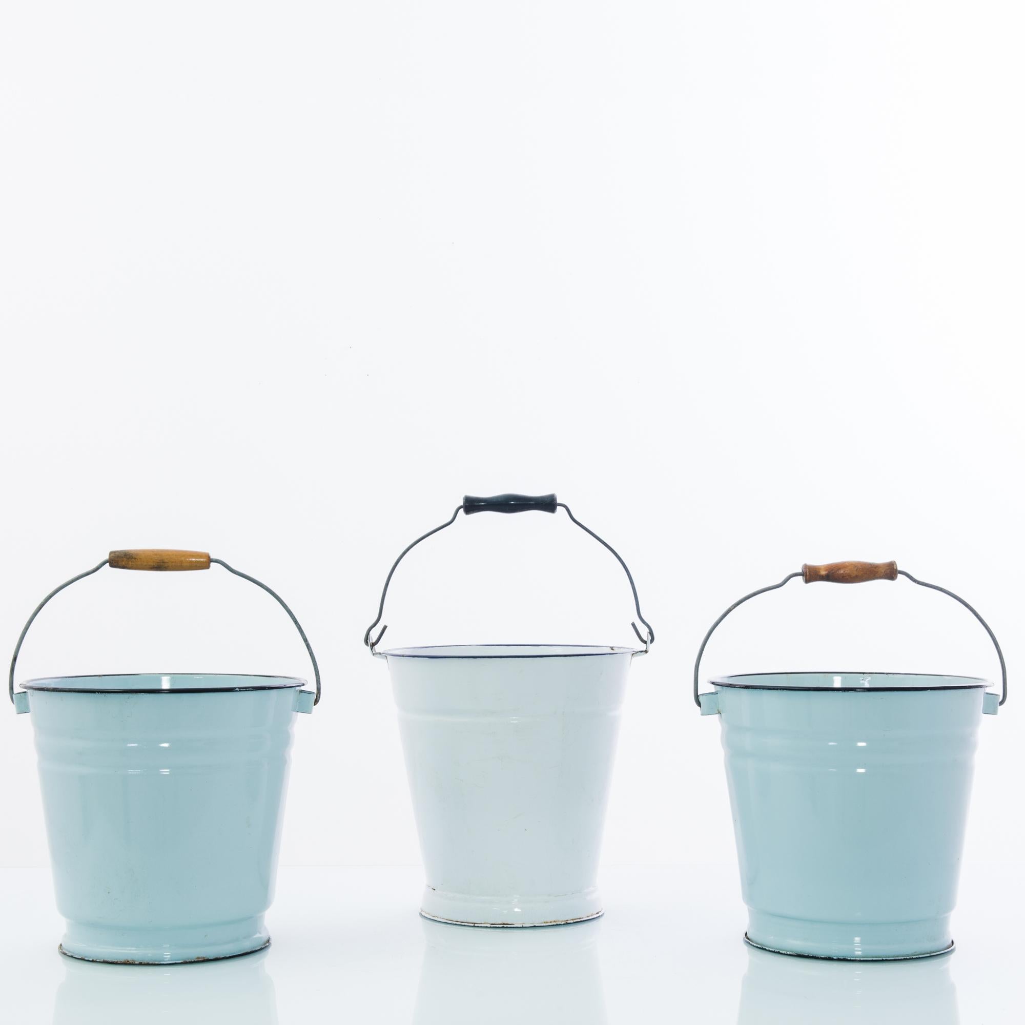 A metal bucket from 1950s Czechia. Bright enamel in pastel hues lends a charming vintage tone to the classic silhouette. The pail is crowned by a handle of metal wire; the wooden handgrip is worn to a patinated shine through use. Nostalgic yet