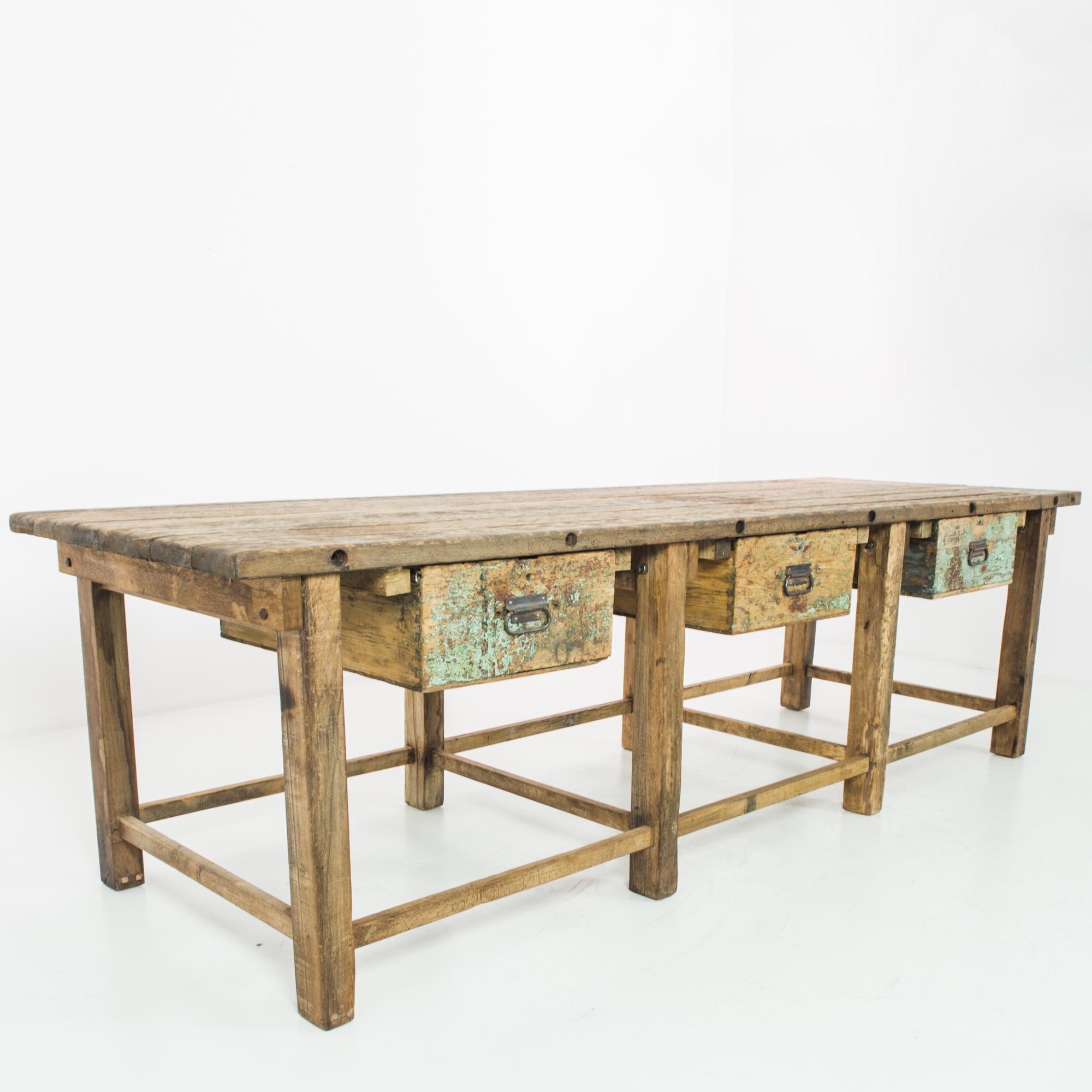 A wooden table from Czechia, produced circa 1950. A work table straight from a mid-century workshop; standing on eight legs, it’s split into three sections around its three sliding drawers. With traces of original patination, nicks, and scars from