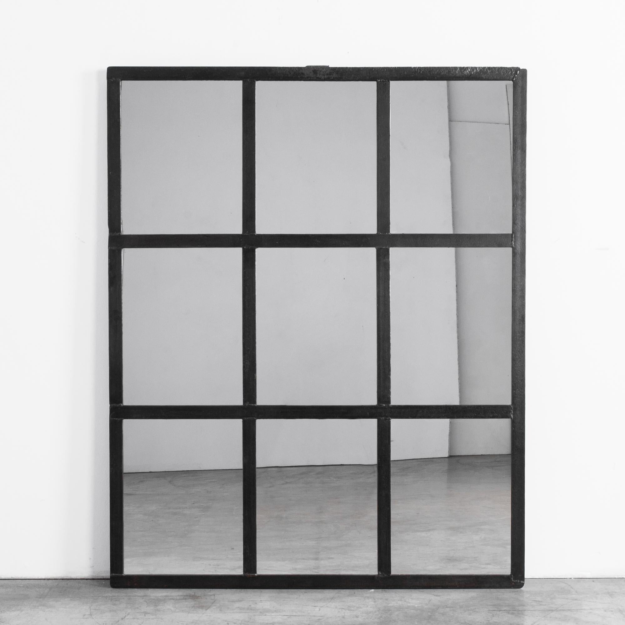 A floor mirror with a metal frame repurposed from a 1950s Czech factory window. A three by three grid of cast metal is fitted with panes of mirrored glass. Purpose built, the rigid lines and dark color of the frame emphasize the post-industrial