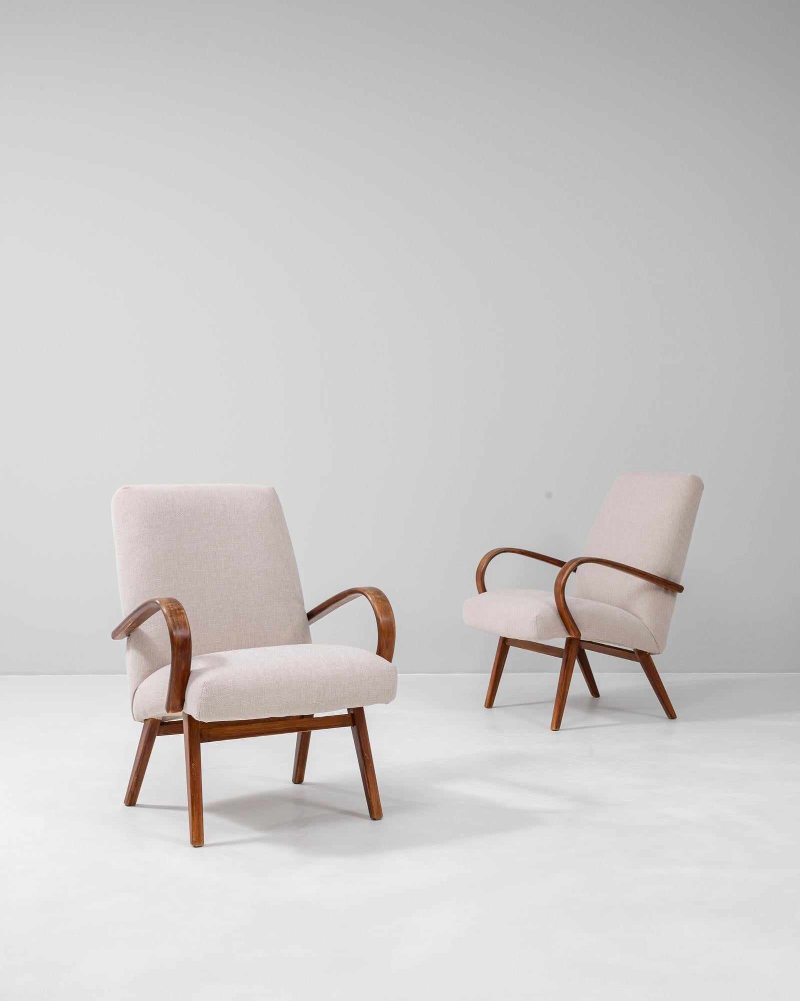 This pair of 1950s Czech upholstered armchairs by renowned designer Jindřich Halabala showcases the refined balance of comfort and modernist form that defines his work. Each chair features gracefully curved wooden arms crafted from bentwood, a