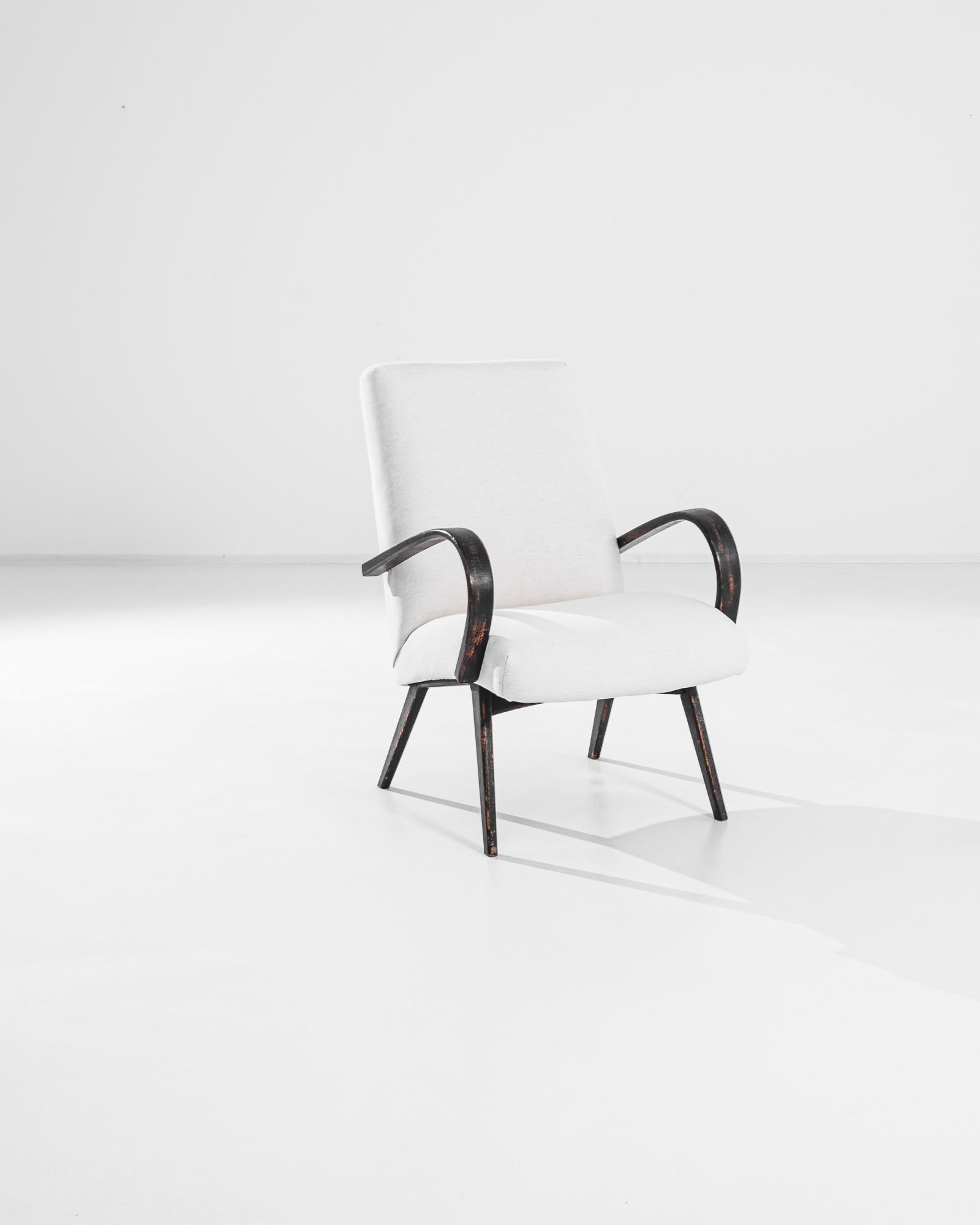 Step back in time with this elegant 1950s Czech Upholstered Armchair. This vintage piece features a beautifully curved wooden frame with a distressed black finish that exudes mid-century charm. The soft, cream-colored upholstery provides a striking