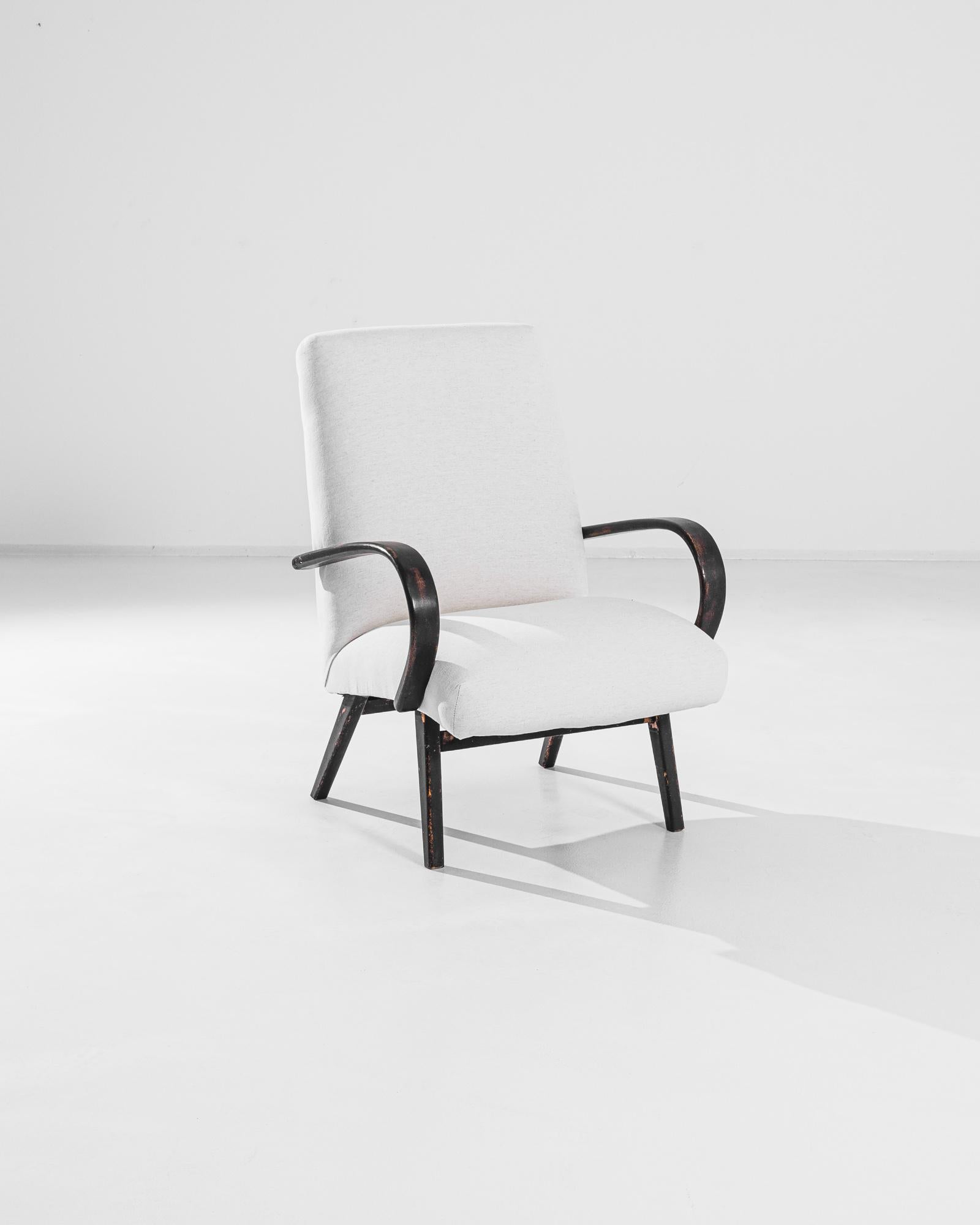 Embrace vintage sophistication with this stunning 1950s Czech Upholstered Armchair. This mid-century gem features gracefully curved wooden armrests and legs with a beautifully distressed black finish, adding character and charm to any space. The