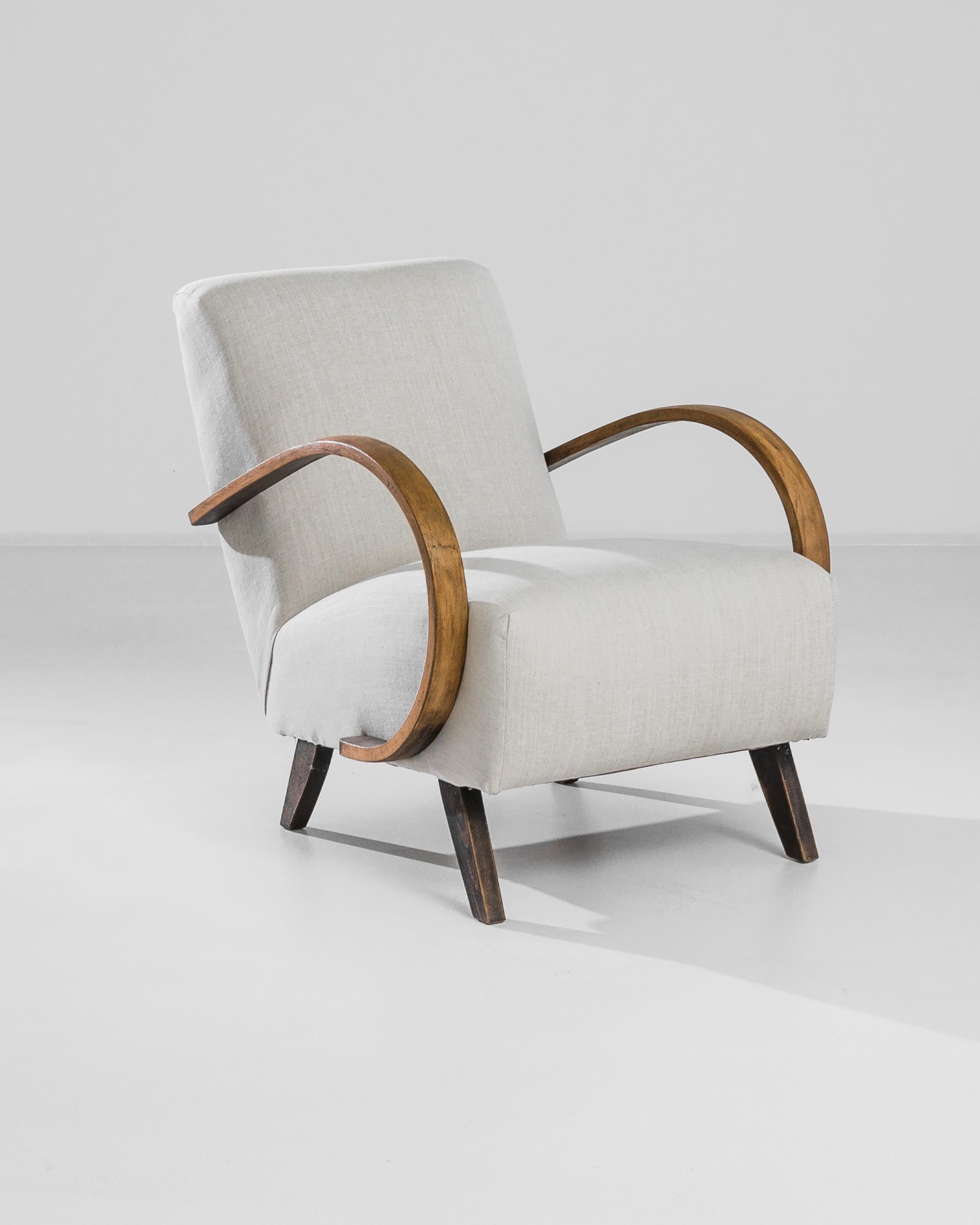Timeless comfort meets Modernist sophistication in this iconic design by Czech furniture designer J. Halabala. Produced in the 1950s, this wooden armchair flaunts an anatomy constituted by contrast: the sweeping curve of the bentwood armrest is
