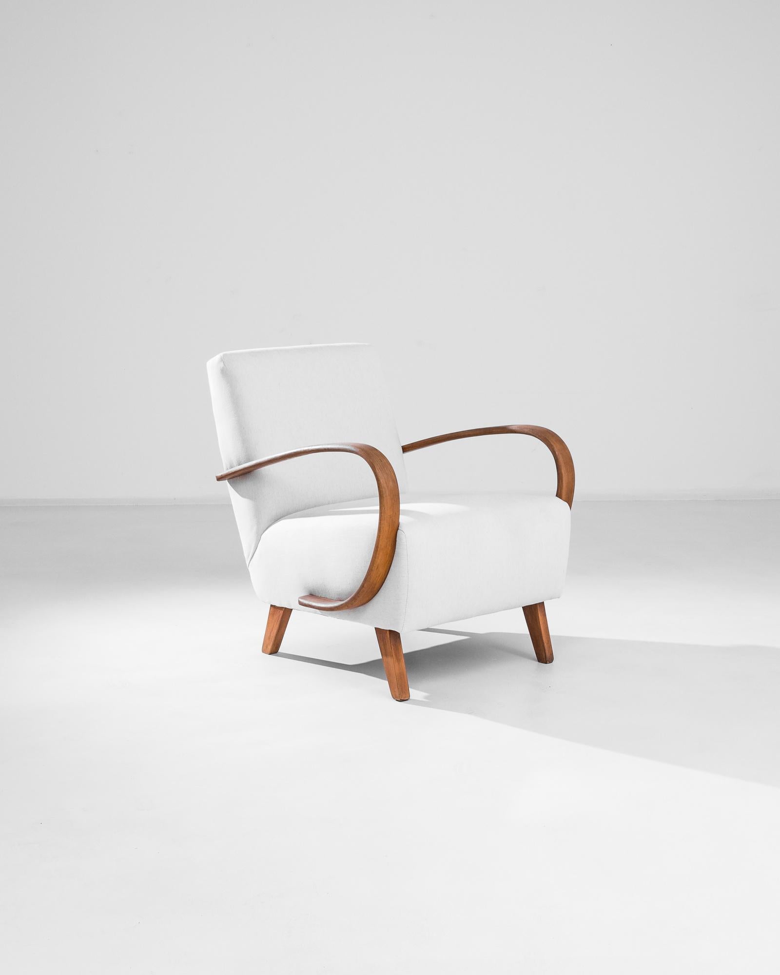 Embrace the iconic design of the 1950s with this exquisite Czech Wooden Armchair by J. Halabala. This beautifully crafted piece showcases Halabala's signature curved wooden armrests, adding a touch of elegance and fluidity to any room. The chair is