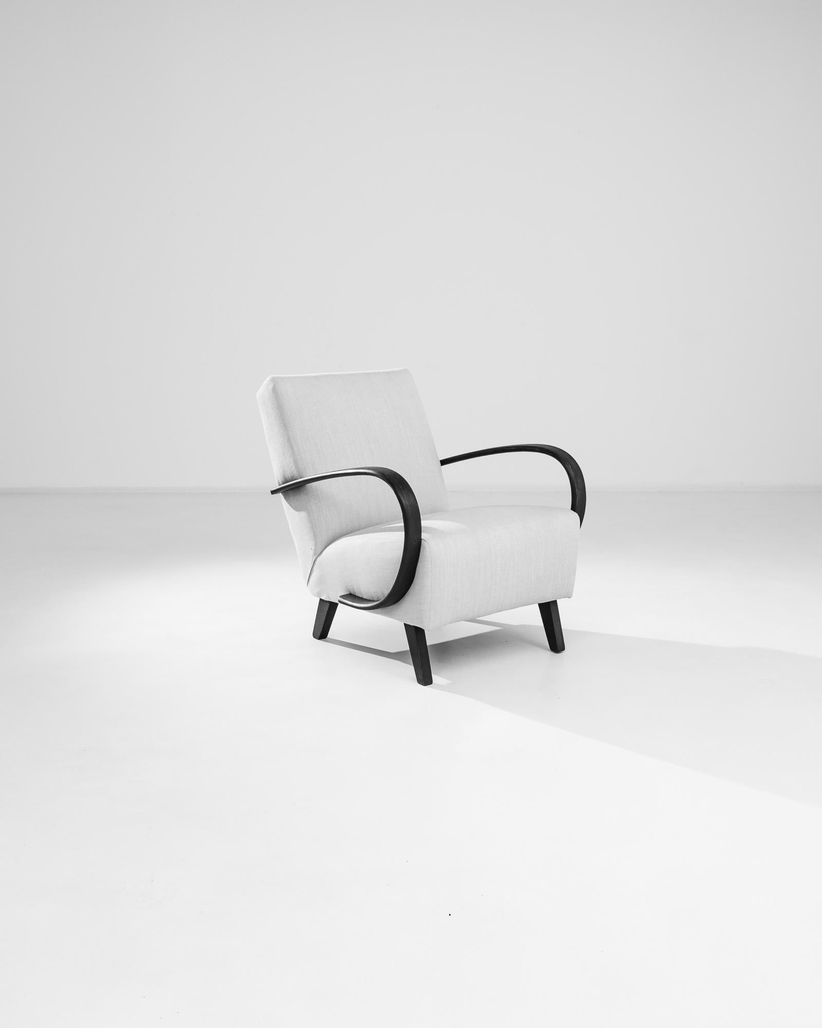 Add a touch of mid-century modern elegance to your home with this 1950s Czech Wooden Armchair by J. Halabala. Renowned for his distinctive designs, Halabala combines sleek black wooden armrests and legs with a plush, light grey upholstery, creating