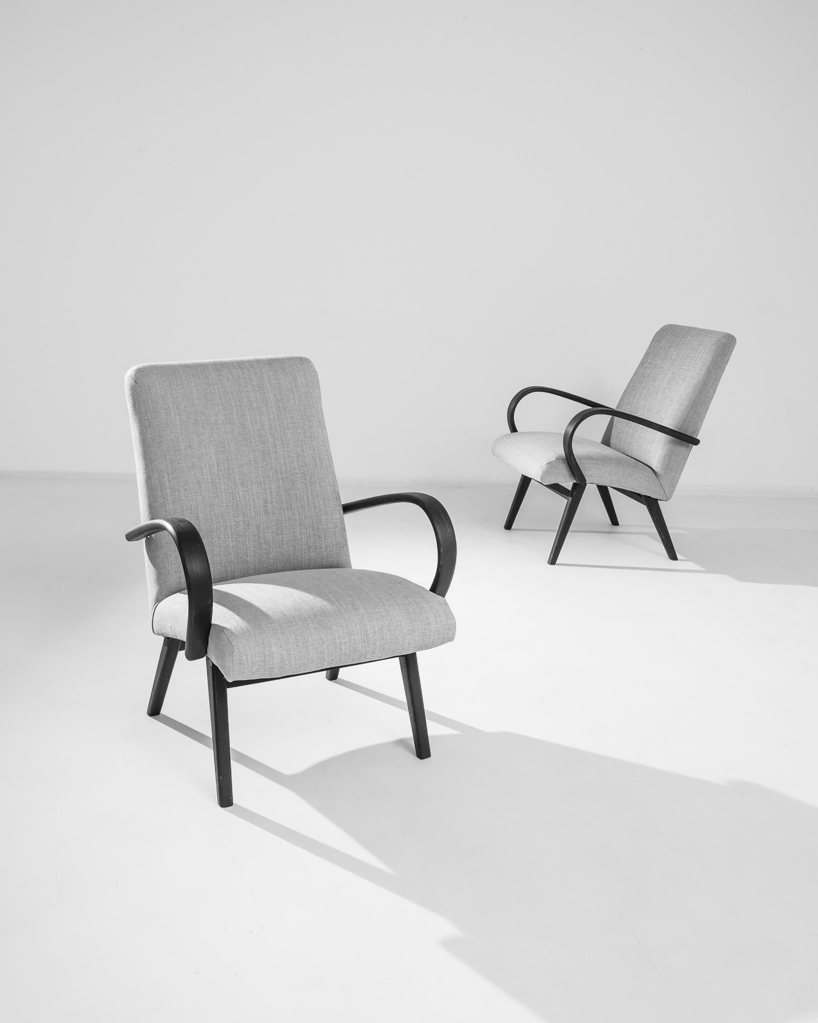 A pair of armchairs by Czech furniture designer Jindrich Halabala. This 1950s design is upholstered in an updated gray fabric, the soothing heather tone was chosen to compliment the sleek black hardwood frame. Influenced by Modern and Art Deco