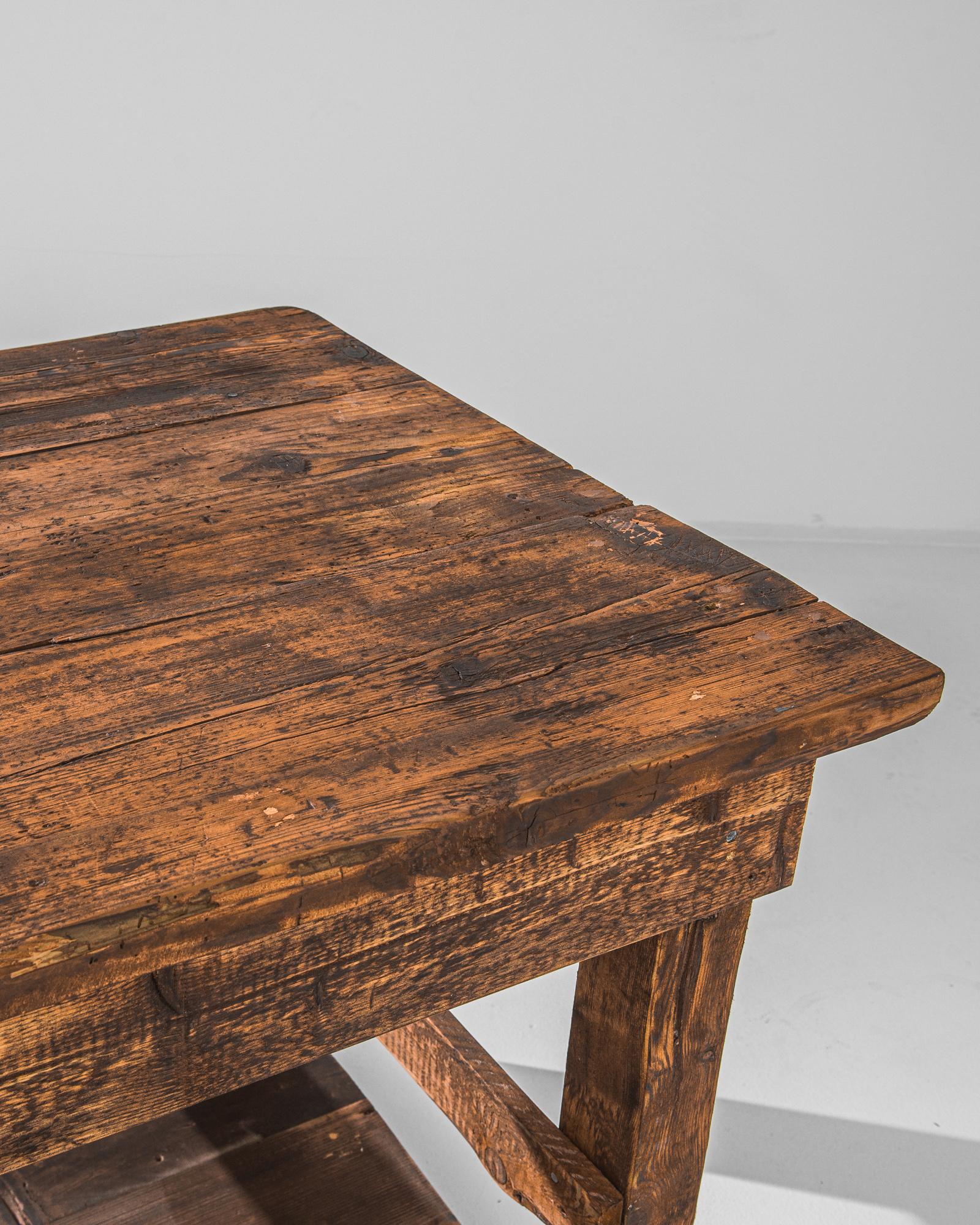 A wooden table from Czechia, produced circa 1950. A vintage work table rustically constructed, nicked with scars of a long lifetime of usage, featuring a three plank tabletop and a lower storage shelf. Sturdy and broad, this piece is supported by