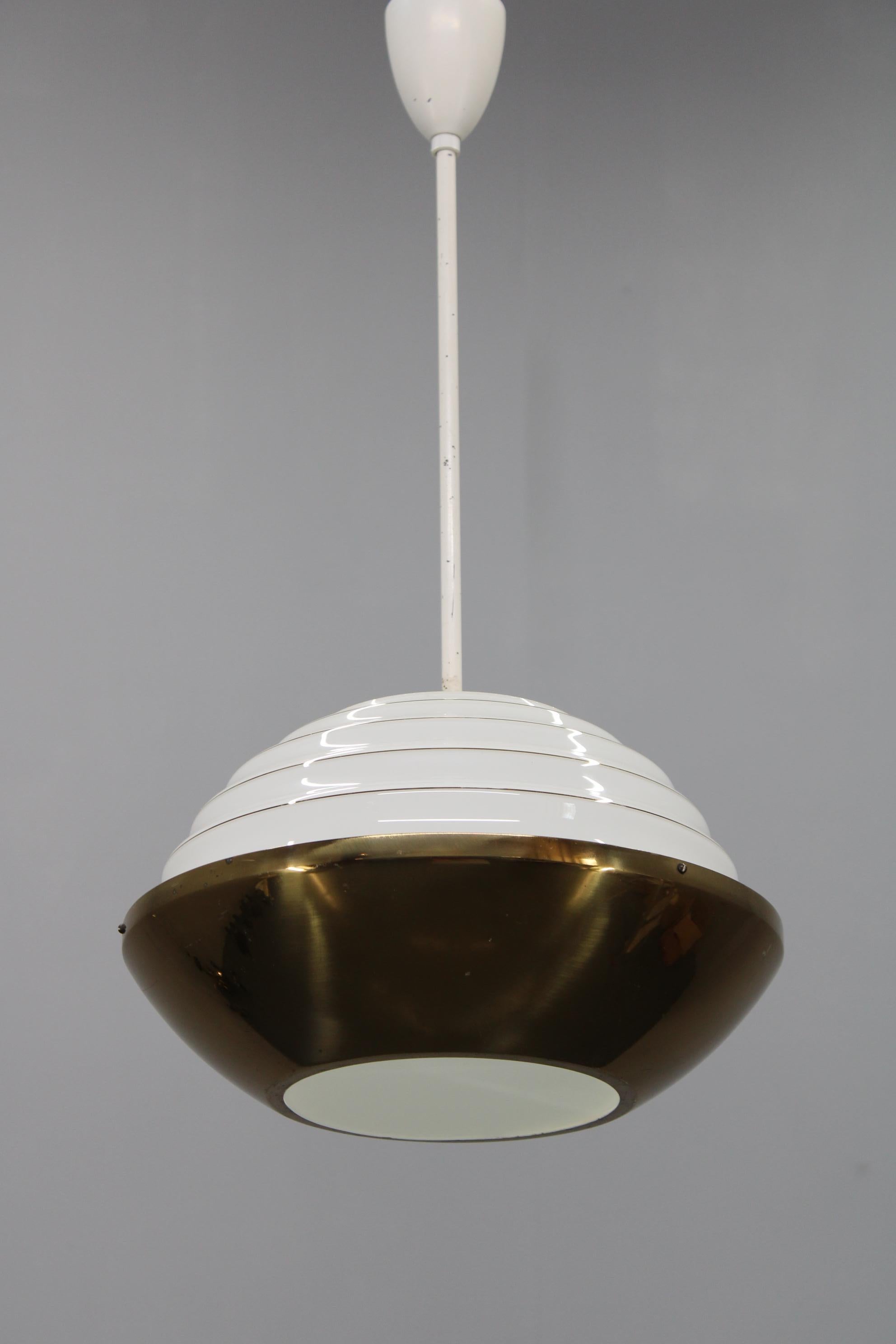 Une suspension raffinée des années 1950 produite en Tchécoslovaquie, combinant un dôme inférieur plaqué laiton avec une structure supérieure en métal blanc à gradins et un élégant diffuseur en verre laiteux opalin. Le design reflète les tendances