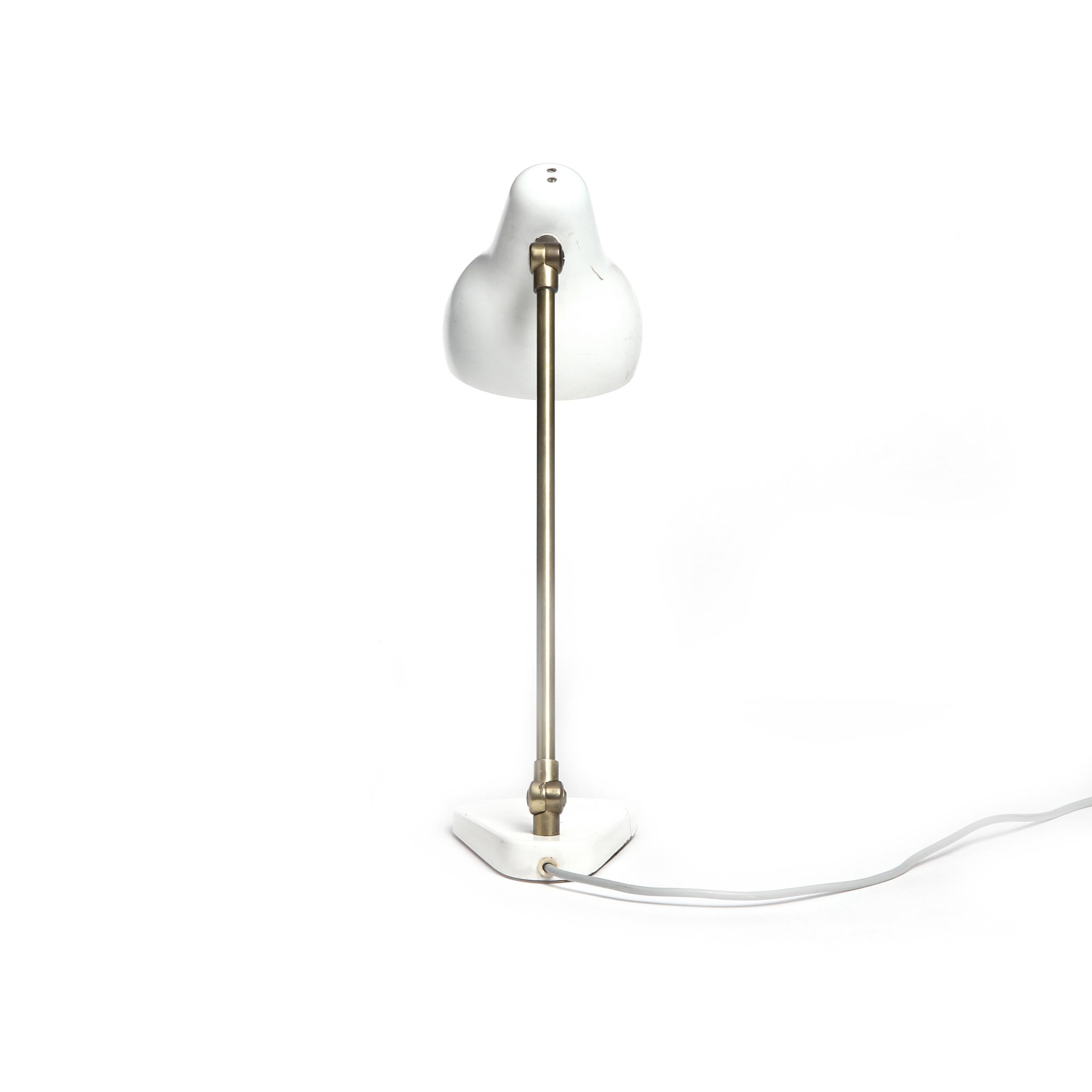 An articulating desk lamp having a brass stem with patina and off-white enameled hood and base.