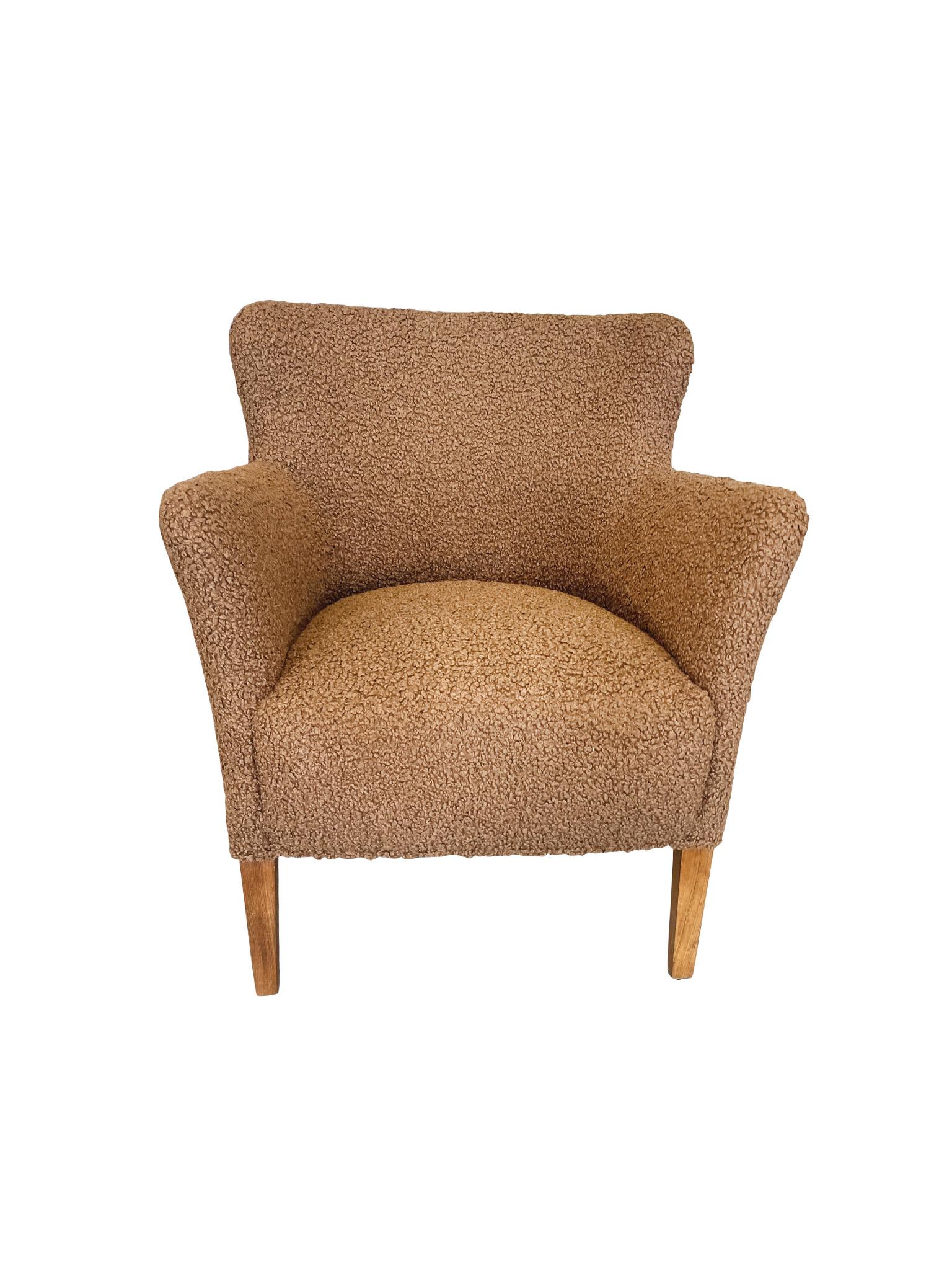 Structurally, this small 1950s Danish lounge chair by Birte Iversen is designed with a low back that curves slightly inward, rounded corners, and high legs crafted from beech wood. It has been newly reupholstered in a richly textured caramel bouclé