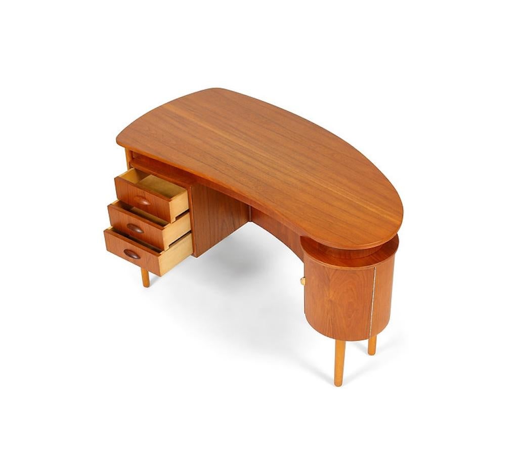 Here is a cool Danish Modern teak desk, probably circa the late 1950s. It has a kidney shaped top, a circular bar cabinet, and a bookshelf and storage on the back. The teak desk sits on solid oak tapered legs. It is a great design and is attractive