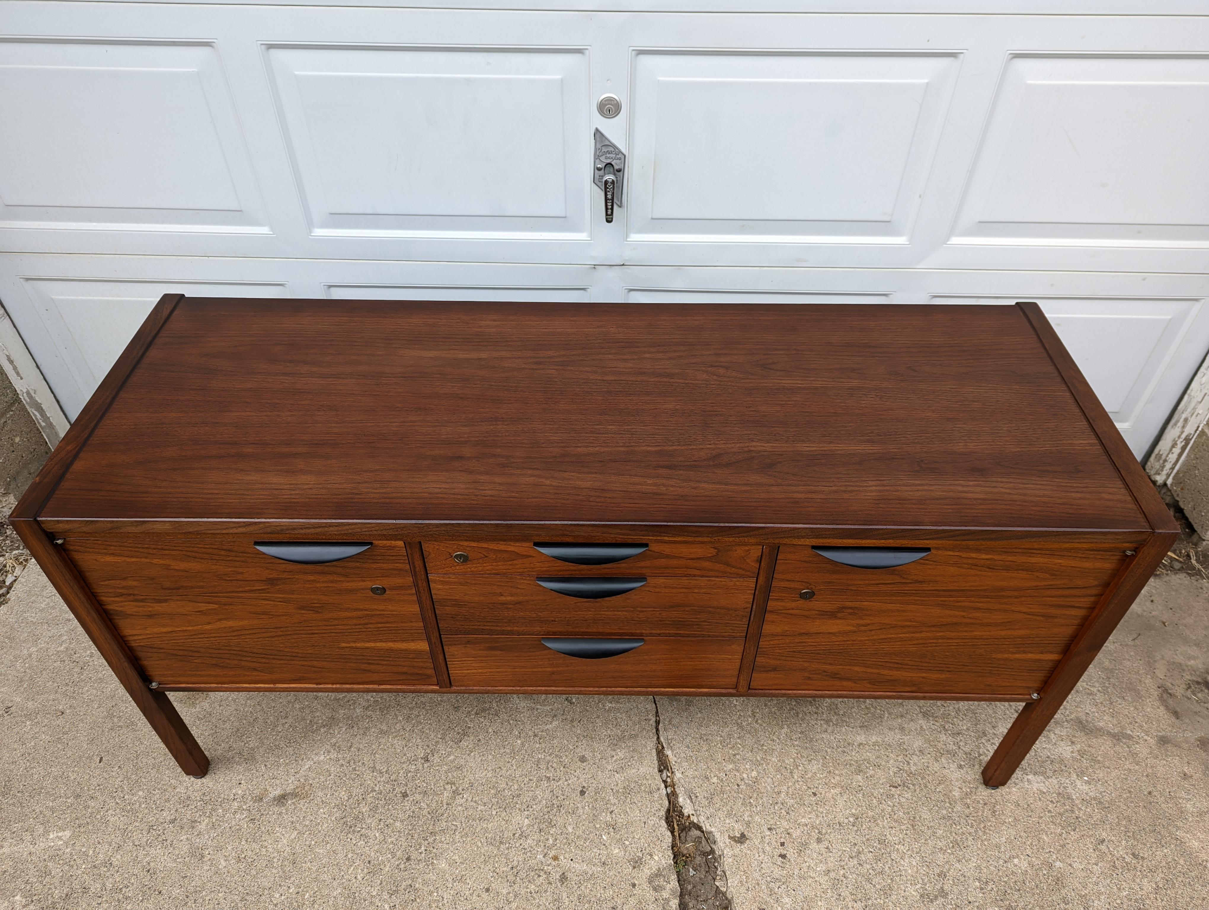 1950s Danish Modern credenza in walnut by Jens Risom.

Excellent condition for its age. Nice walnut grain and figure. Black aluminum pulls.

3 Central drawers flanked by doors that open to compartments. One adjustable shelf. Adjustable