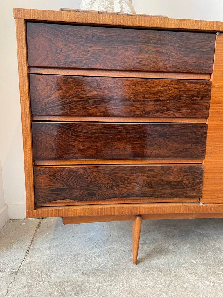 Danish solid rosewood and mahogany extra long sideboard with four storage doors, four sliding doors accompanied with wood and glass shelving, and mirrored bar with lighting. The sideboard also features modern legs and brass detailing.
  