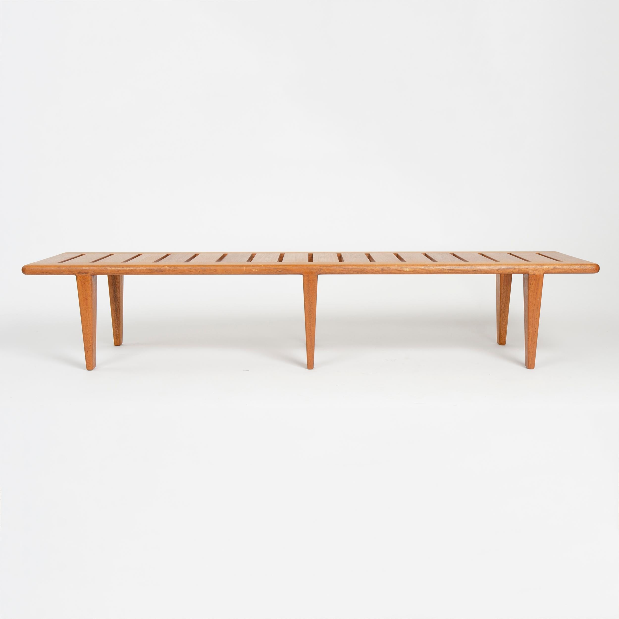 A solid teak bench with a slatted seat over six (6) tapered legs.