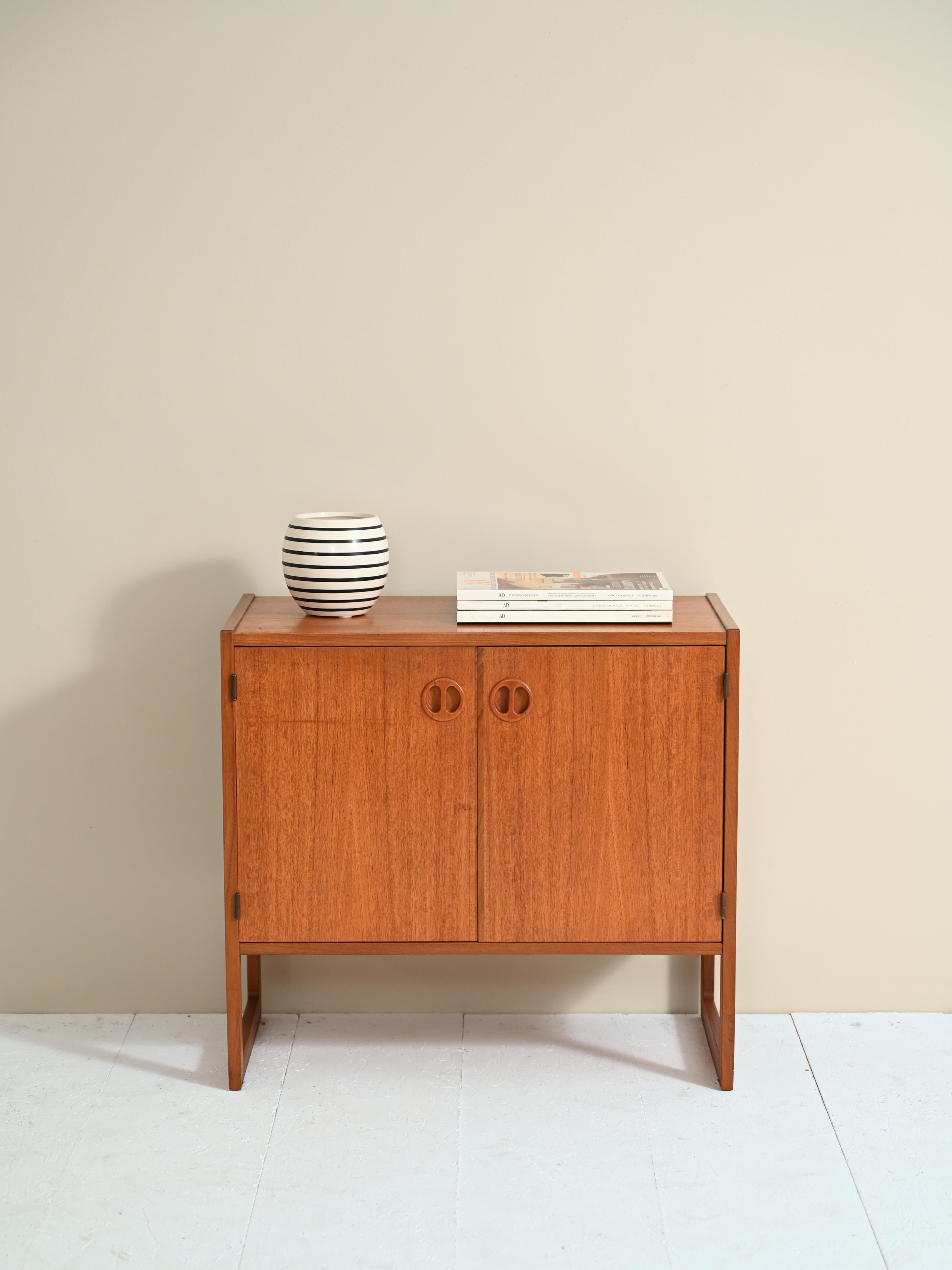 Sideboard originale anni ’50 con ante a battente e impugnatura scolpita nel legno.

Mobile di manifattura nordica con un vano dotato di mensola. Caratterizzato dalle marcate venature e dal colore dorato del legno teak.

Le dimensioni contenute