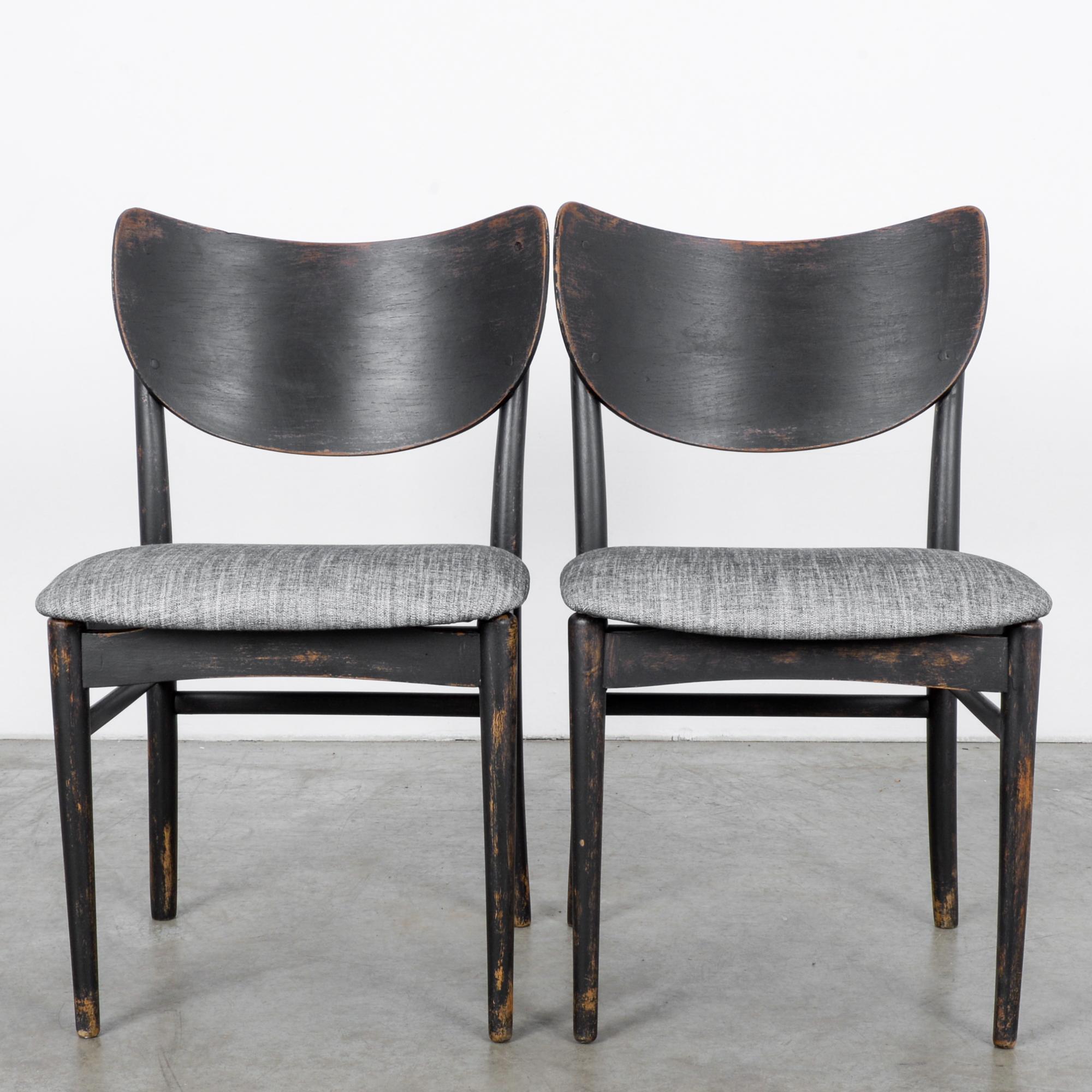 This pair of wooden chairs with newly upholstered gray seats was made in Denmark, circa 1950. The black frames display a beautifully worn patina, hinting at the warm tones of the wood. With the elegantly curved backrests and angled rear posts, these