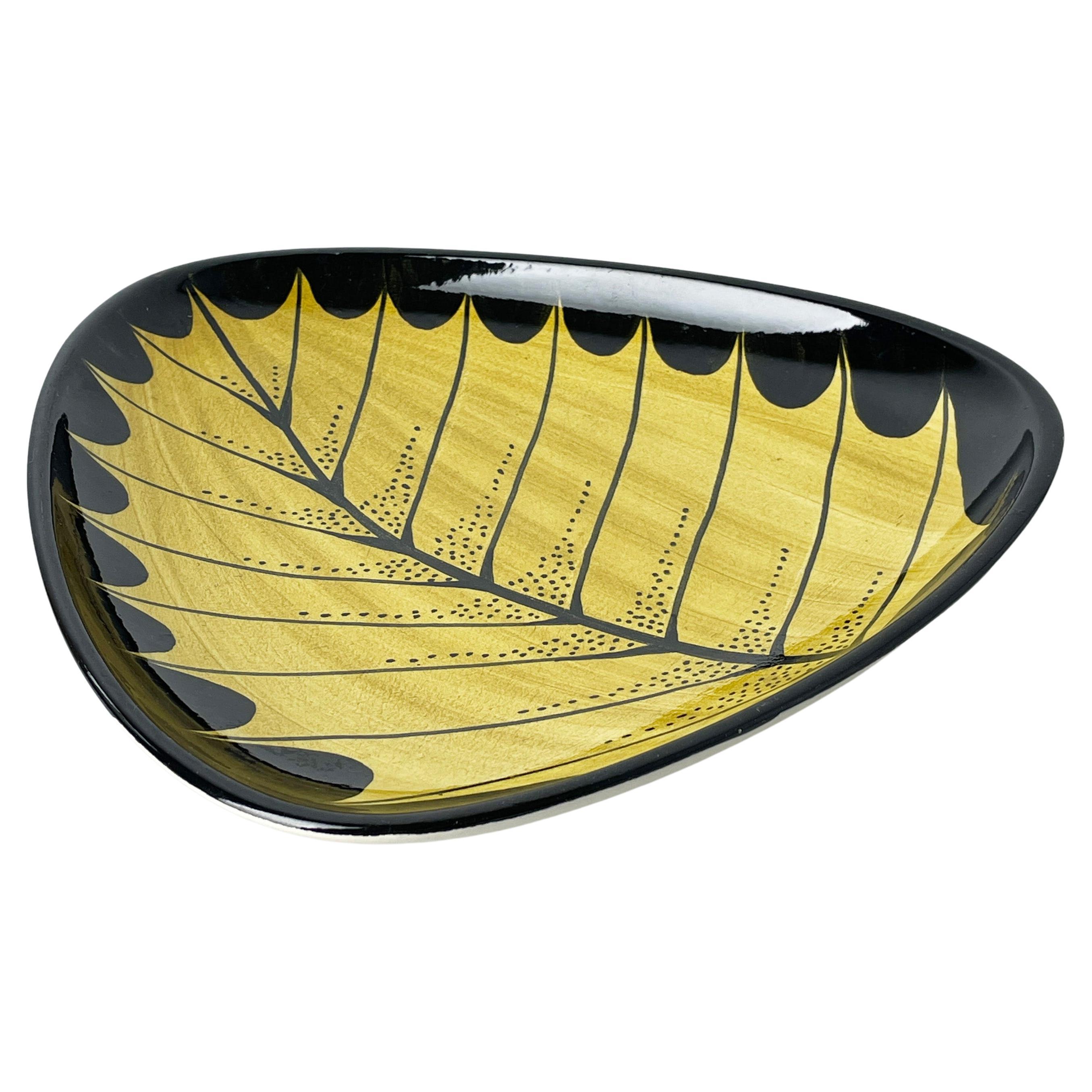 Bol / assiette décoratif en céramique de forme triangulaire produit entre la fin des années 1950 et le milieu des années 1960. Il est orné d'un motif de feuilles jaune et noir audacieux. 
Marque du fabricant sur la base : 4022 3