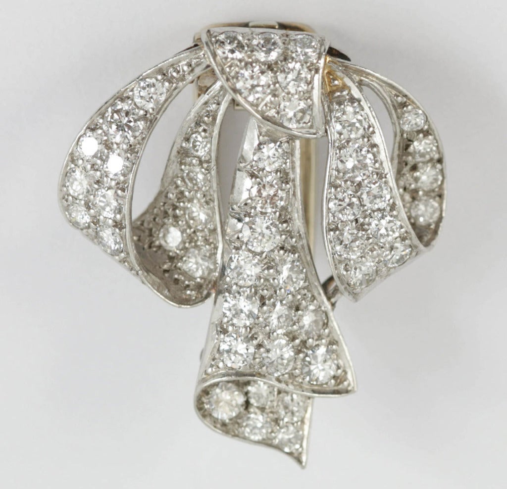 A stylish vintage platinum brooch in the design of a tied ribbon and set with brilliant cut diamonds. Gold double clip fastening.
Measures 25mm in height x 21mm in width.
1950's Vintage piece.
20th century, English circa 1950.

Stock no. 1159