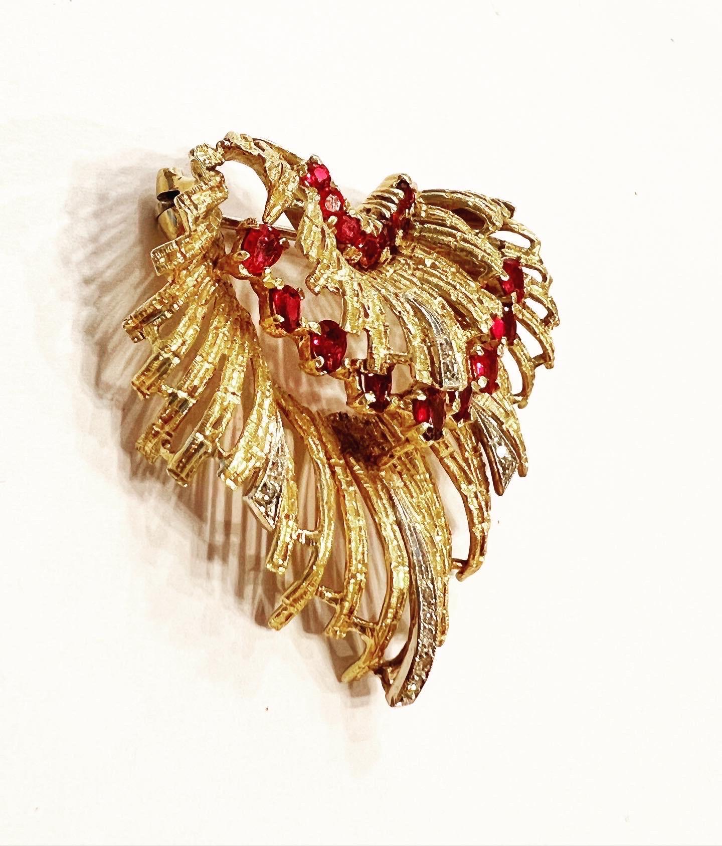 Spilla a conchiglia stilizzata in oro giallo 18 ct. 1950 con diamanti e smeraldi, 
Peso totale approssimativo dei diamanti:  0,11 carati.
Peso totale approssimativo dei rubini:  1,6 carati.
Peso totale del gioiello: 13.34 g.
Condizioni