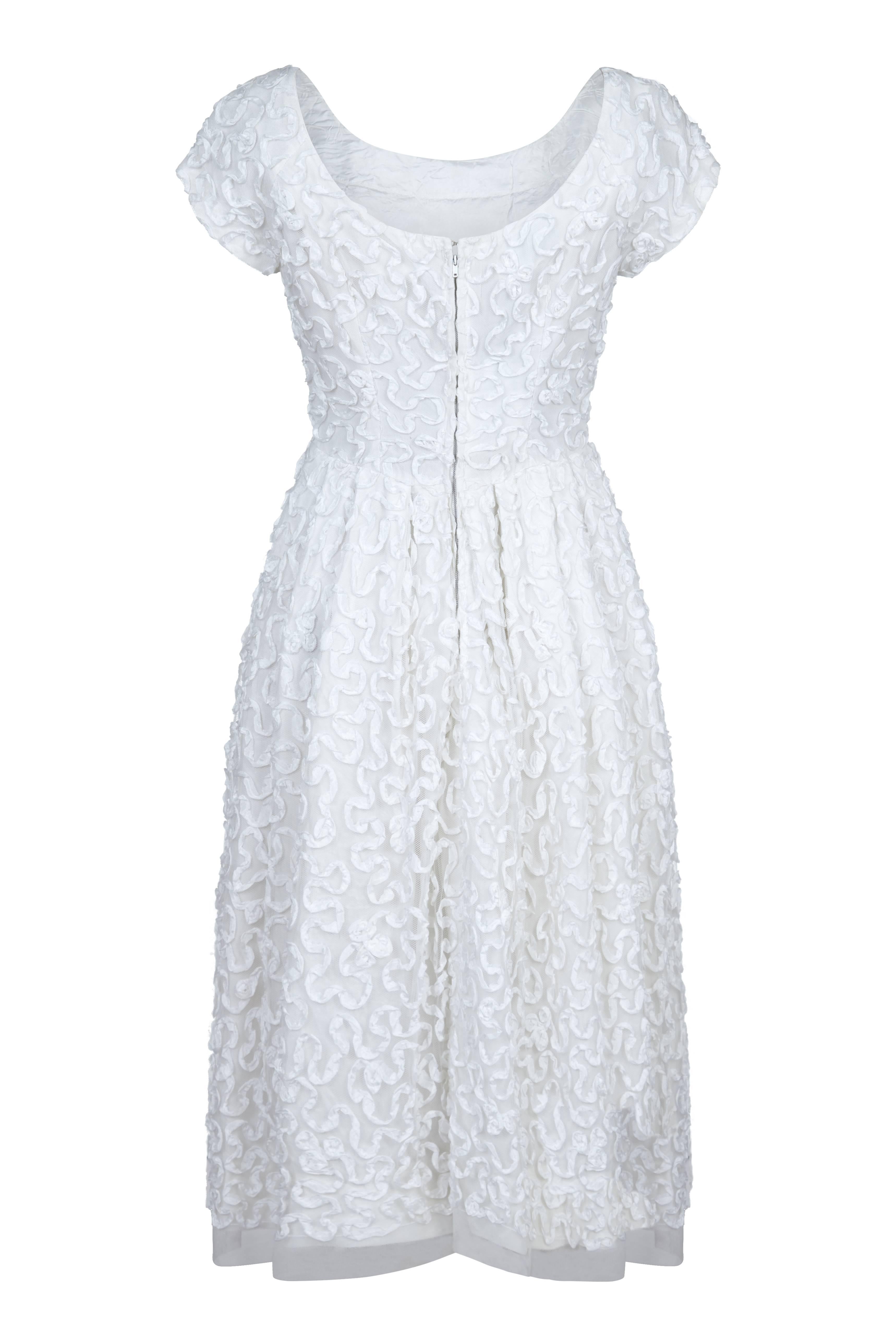 A beautiful and timeless original 1950s pure white tulle ribbon appliqué work dress from high-end British boutique label Diana Warren.  Classic scoop neck, cap sleeves, a fitted bodice and pleating to the waist, the dress is adorned all over in