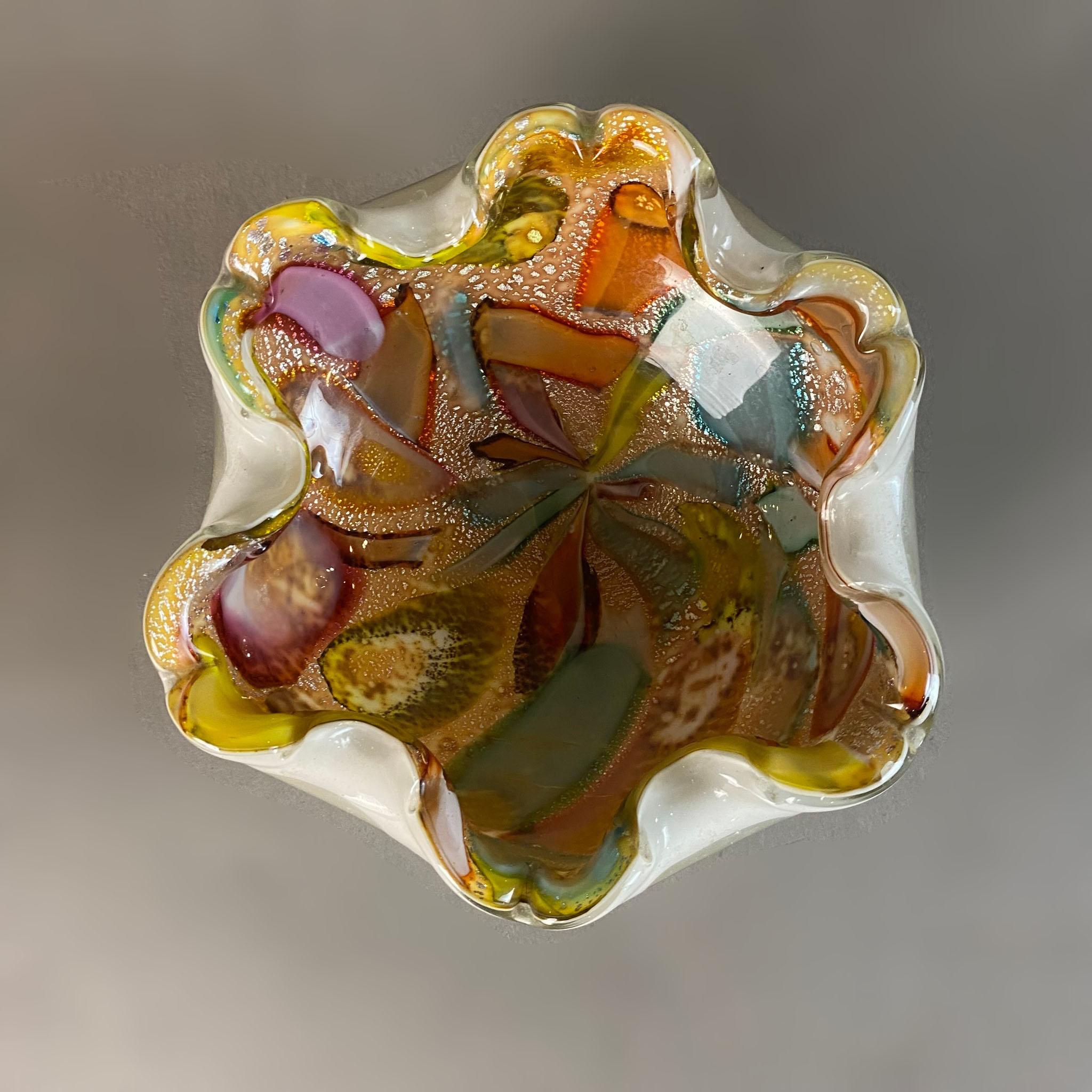 Ein italienischer Aschenbecher aus geblasenem Murano-Glas aus den 1950er Jahren von Dino Martens. Der mehrfarbige Aschenbecher hat eine abgerundete  Form mit Wellenschliff und Blattsilberapplikationen im Glas.

Corrado 