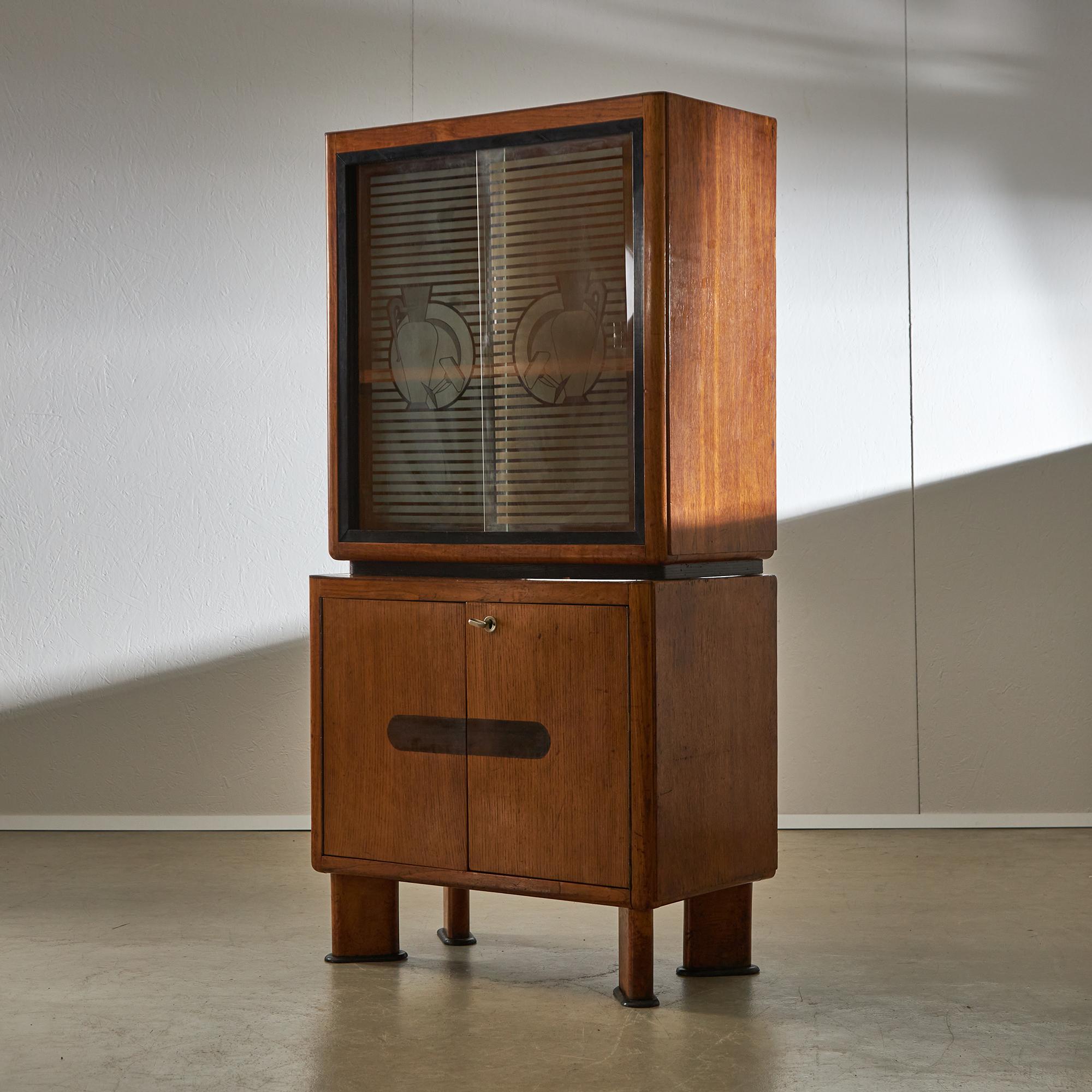 Presentamos una elegante vitrina de los años 50, fabricada en madera de roble, con un diseño armonioso que permite que las secciones inferior y superior se apilen a la perfección sin necesidad de fijaciones. El compartimento inferior cuenta con