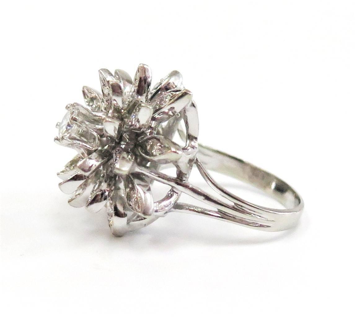 Circa 1950s, this fabulous midcentury 14 karat white gold cluster ring features a central sparkling round brilliant-cut diamond weighing 0.38 carat with an SI clarity and G-H color. Accenting the central stone in a domed flower motif are twenty-four