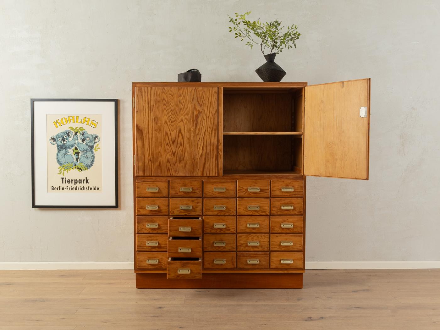 Wonderful drawer cabinet from the 1950s. High-quality corpus made of blockboard in pinewood veneer with 25 drawers, two doors, one shelf, a new top made of plywood and a wooden base.

Quality Features:
very good workmanship
high-quality