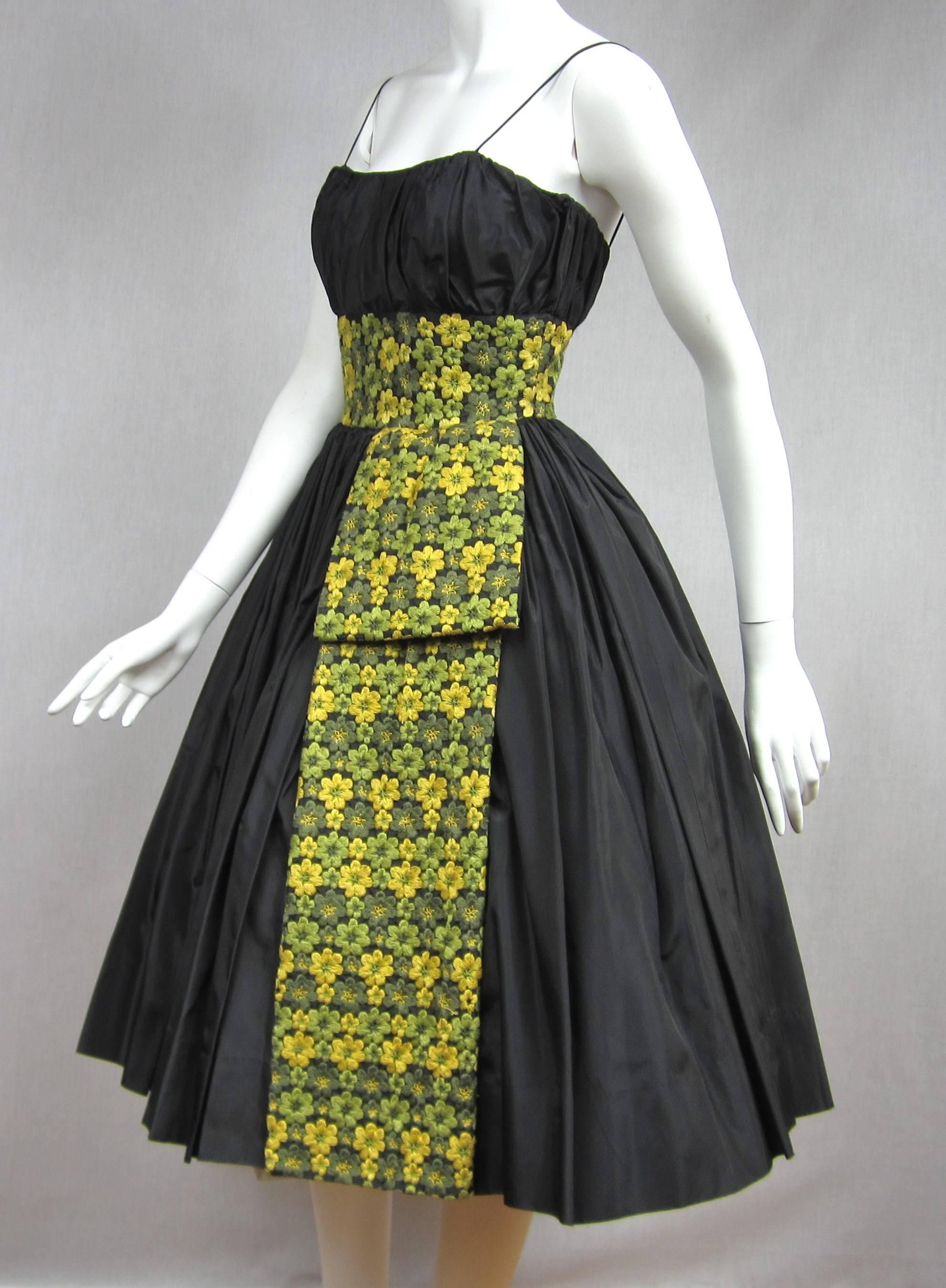 A true Beauty, 1950s Black Taffeta Pleated Bodice Cocktail Dress. It has Boned Bodice with a pleated sexy bust *Pleated Tucked Waist *Large Embroidered Floral Waist that drapes down the side *Labeled SAKS 5th Ave *A Little Black Dress with Loads of