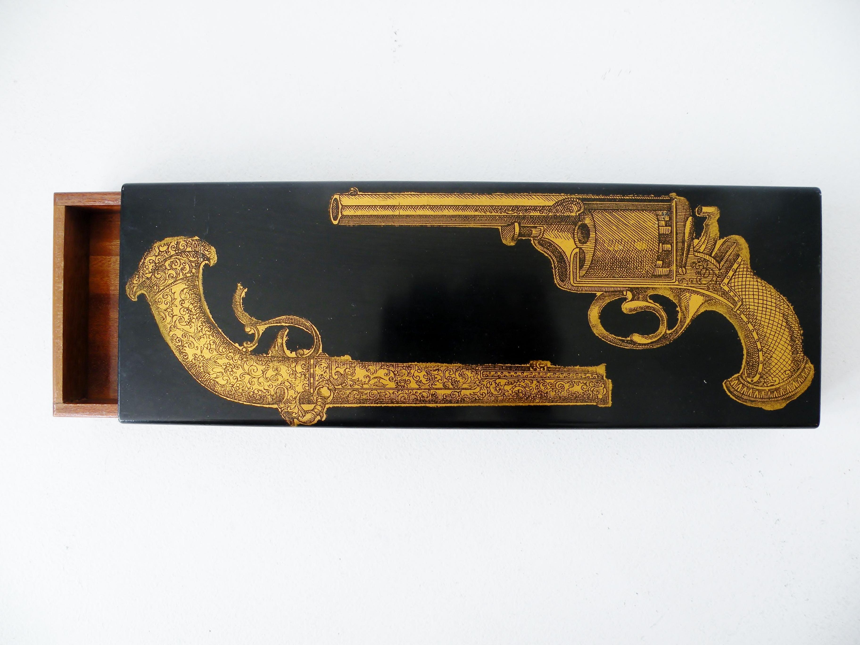 An early enameled metal and mahogany trinket dresser box designed by Piero Fornasetti depicting a pair of pistols. Dates to the late 1950s and made in Italy.