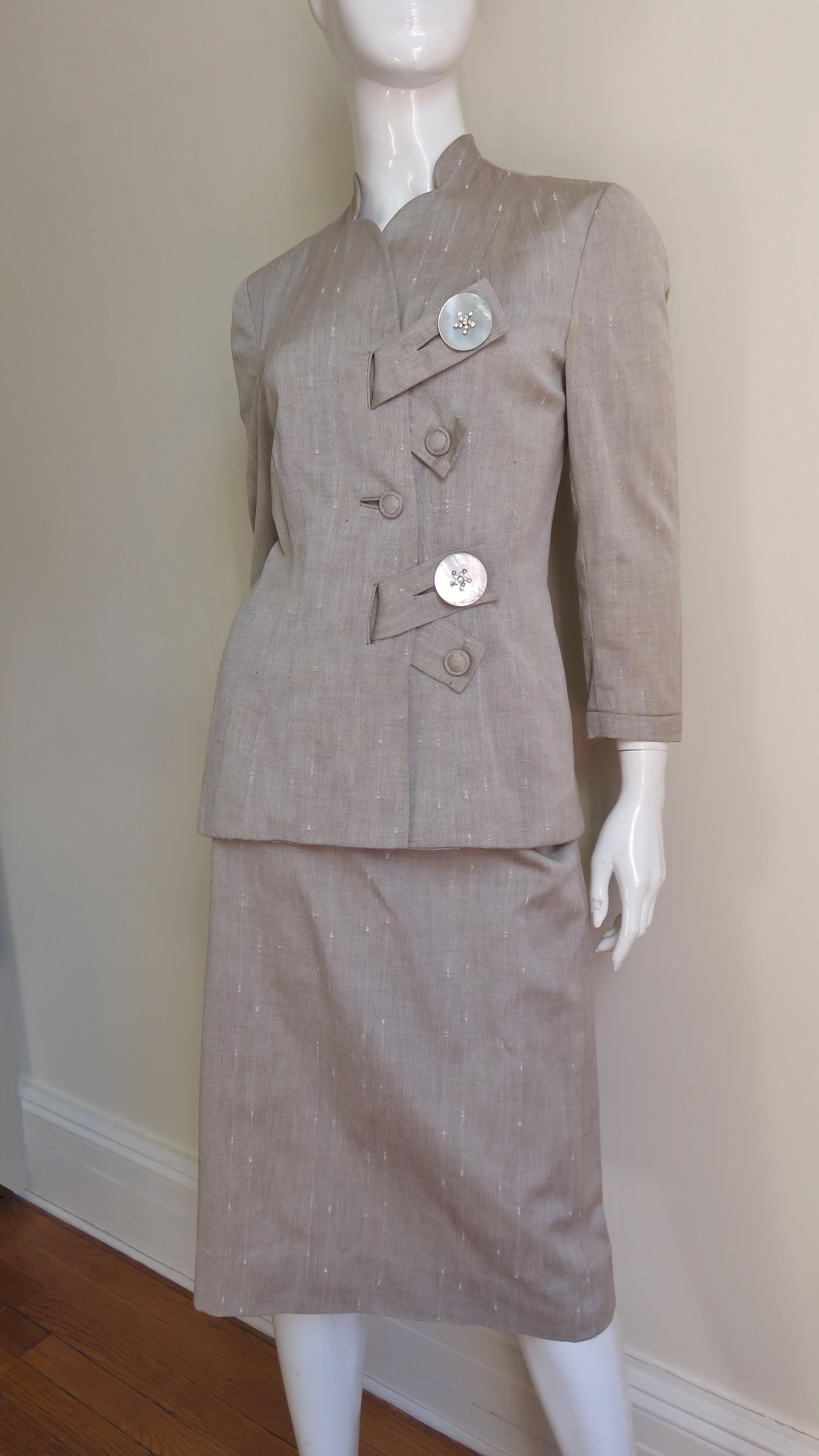 A fabulous suit from Eisenberg Originals in a taupe linen cotton blend.  It has 3/4 length sleeves and a stunning unique front closing via diagonal tabs through bound buttonholes and gorgeous rhinestone incrusted mother of pearl buttons with smaller