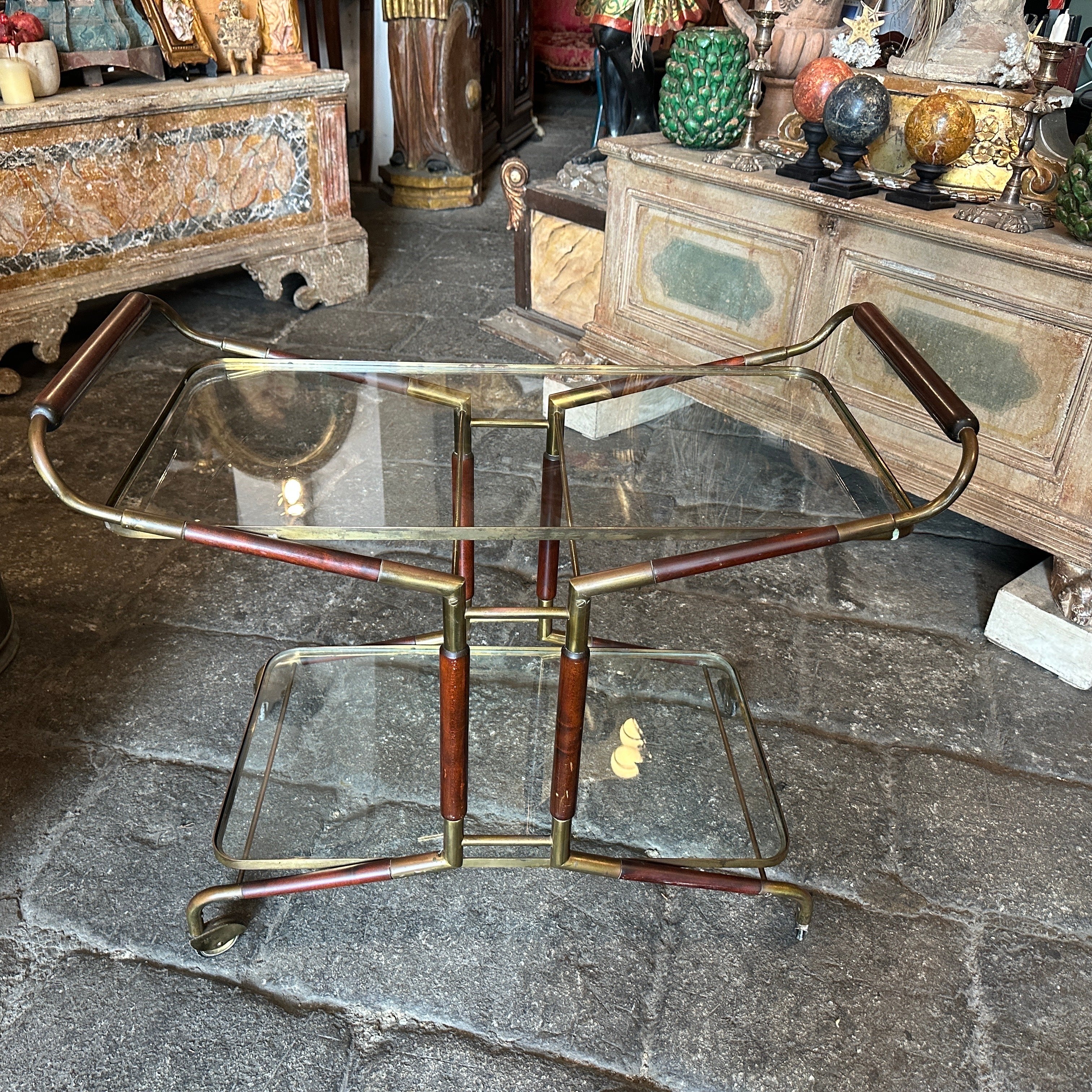 This is a mid-century modern bar cart designed by Cesare Lacca and manufactured in Italy in the 1950s. The design features an elegant combination of materials, including solid brass in original patina, glass, and mahogany wood. The frame is