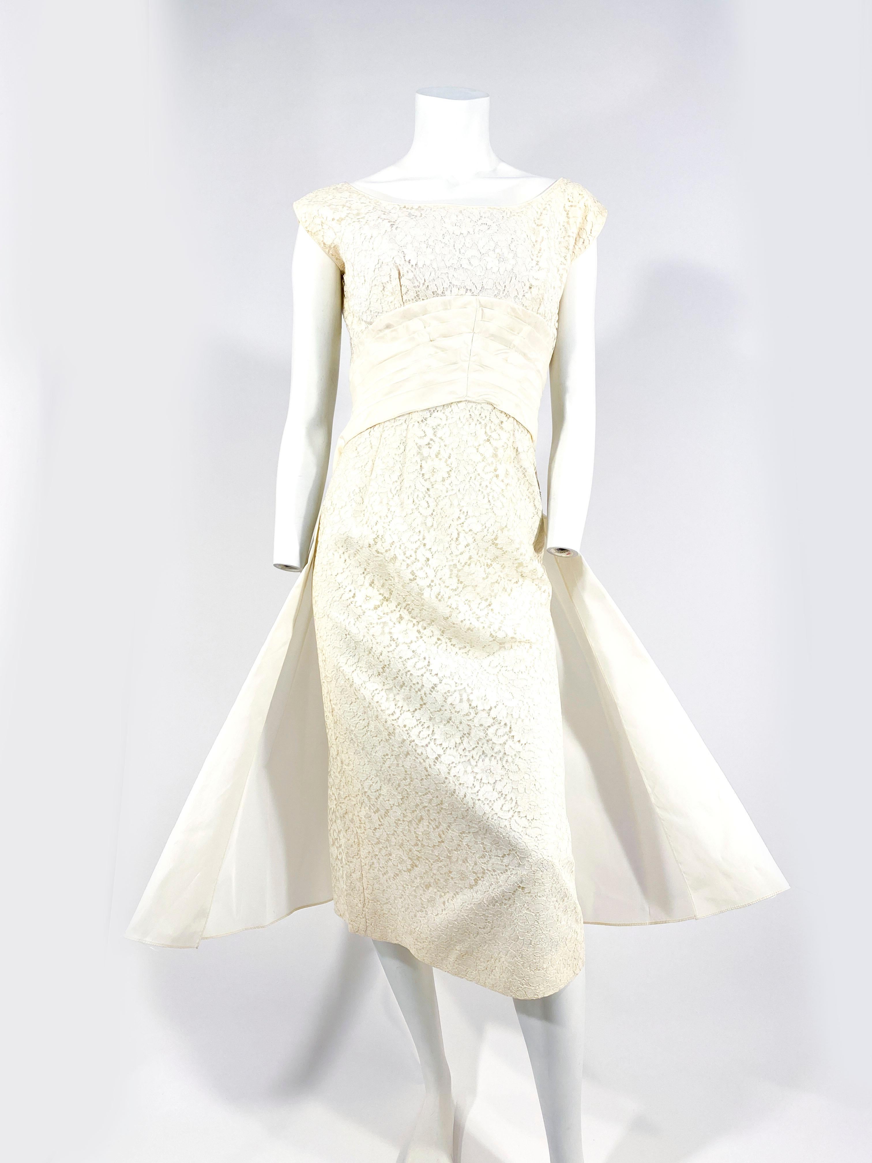 Late 1950s Emma Domb off-white colored lace dress with cap sleeves and full lining. The waist is a hand-pleated taffeta cummerbund that drapes into the back to to full fishtail drape from the back of the waist to the hem of the dress finished with a