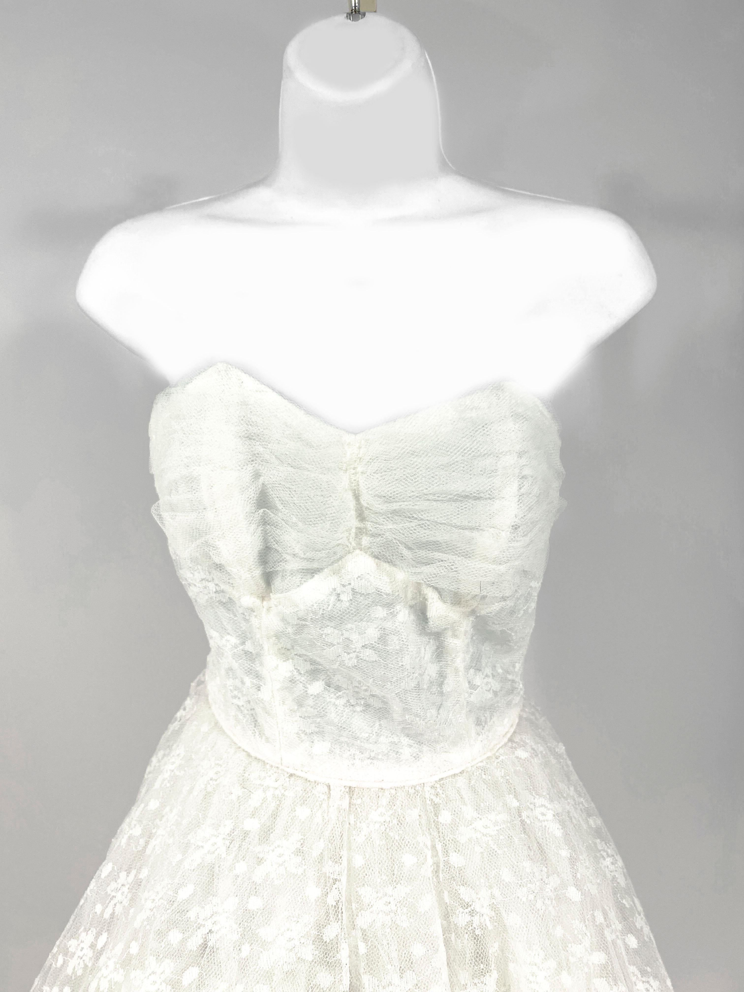 1950s Petit Emma Domb white dress that can be a Prom or a wedding dress. The skirt and bolide is covered in a white polyester lace with a floral pattern. The strapless top is accented with ruched tulle and the back of the skirt has a scalloped drape