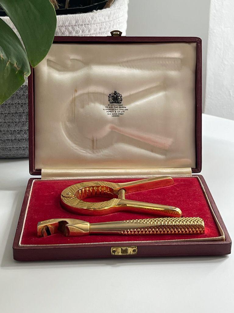A vintage mid-century English bar tool set by Asprey International Limited crafted in the UK. The set includes a luxurious bottle opener and a champagne cork remover and comes in the original Asprey & Company Limited red velvet box. 
Both pieces