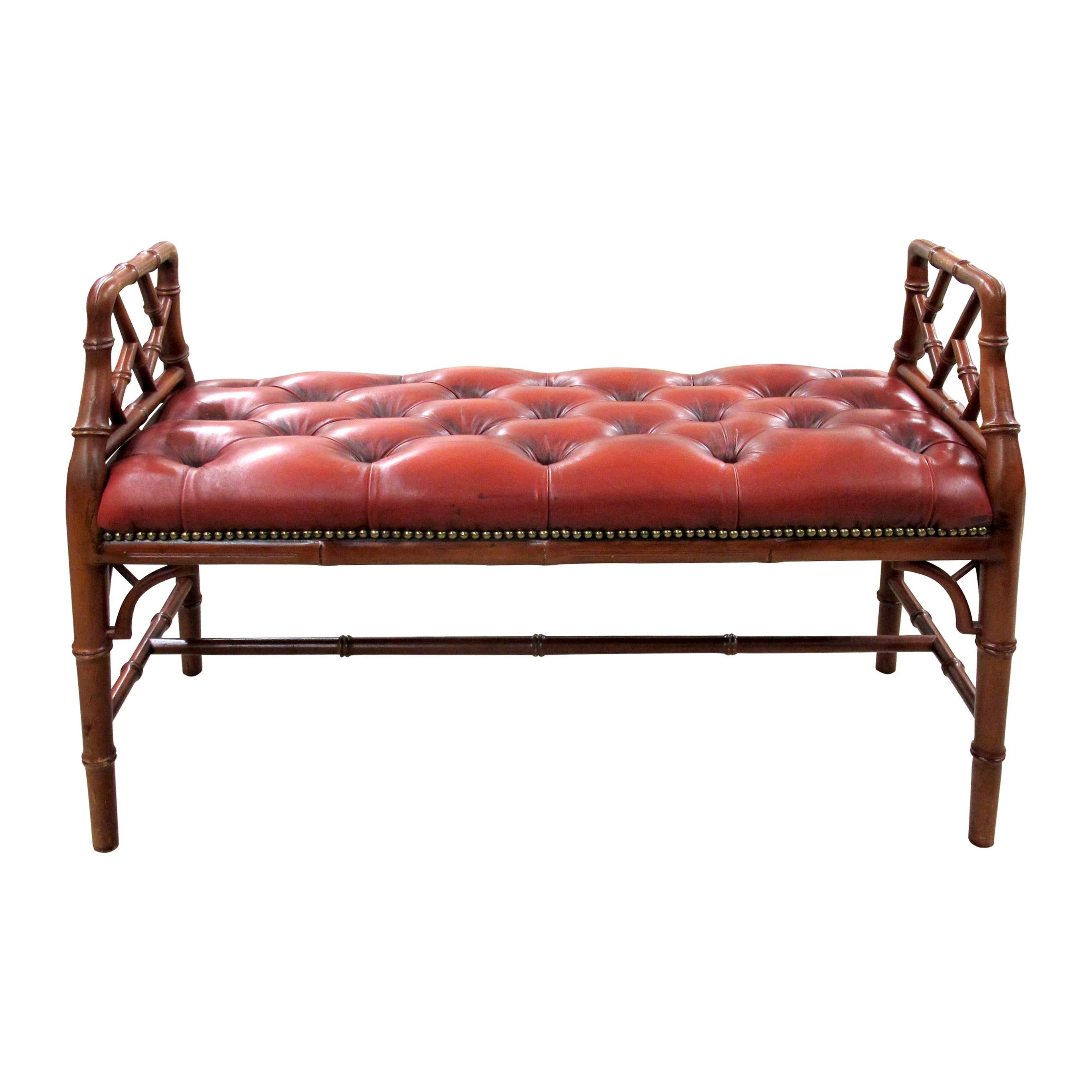 An English mid-century bench, circa 1950, with faux-bamboo hardwood frame and stretcher supports. Upholstered in button-tufted oxblood red leather with brass nail head trim. Raised open arms with lattice detail. Solid and decorative, suitable for