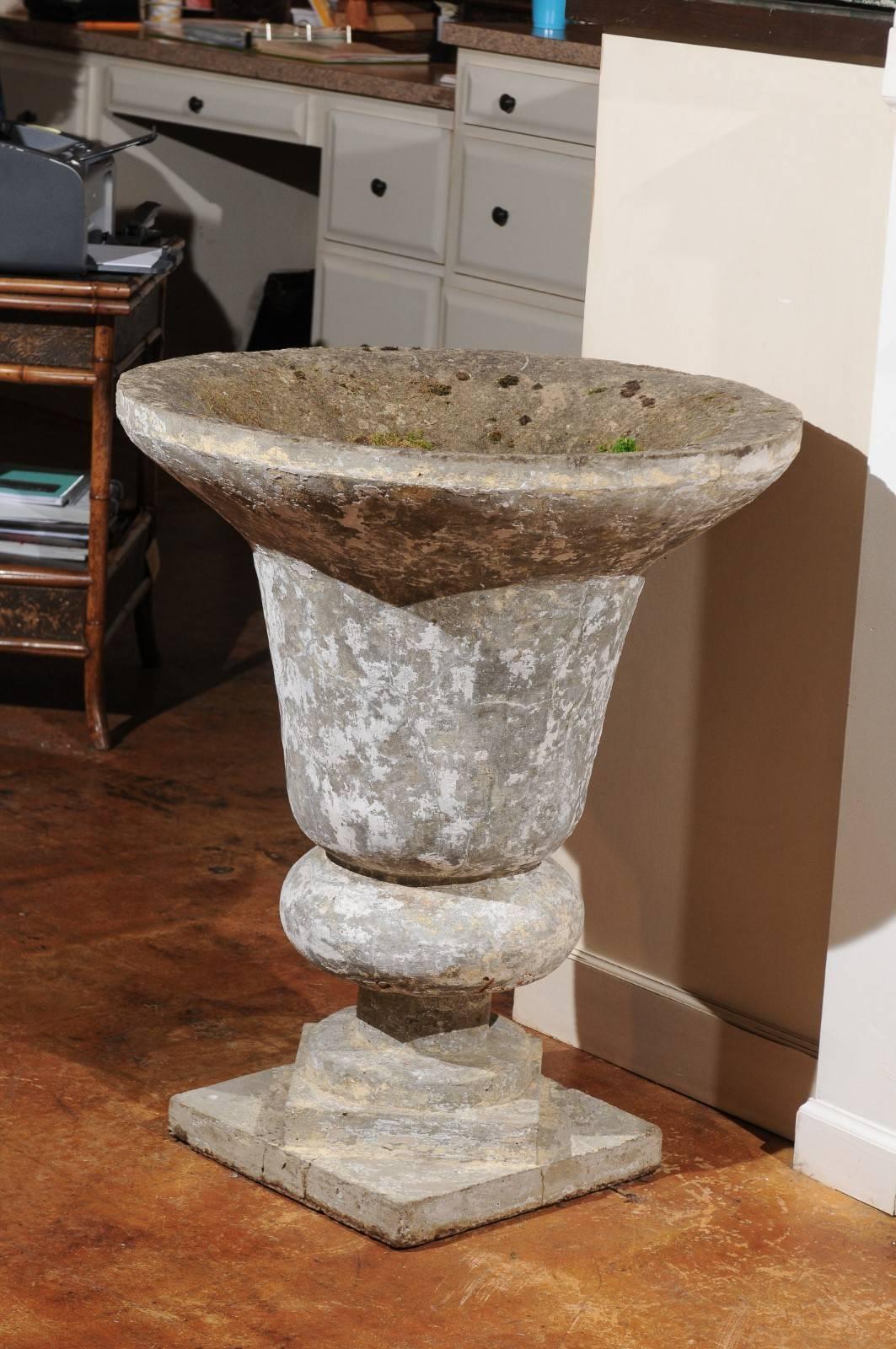 An English tall vintage stone urn raised on catty-corner square bases from the mid-20th century, with nicely weathered appearance. This English stone urn features an exquisite inverted bell shape with large lip in the upper section, raised on an