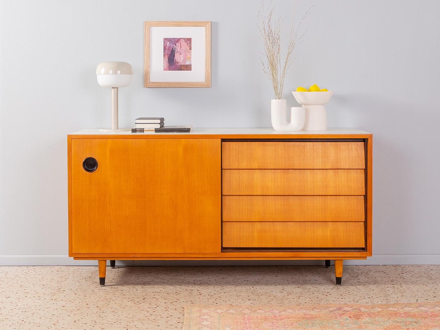 Rare sideboard from the 1950s by Erich Stratmann for the Oldenburger Möbelwerkstätten. Corpus in ash veneer with four drawers, one sliding door, one shelf and cigar shaped feet. The top is coated with creamy white formica.

Quality Features:
