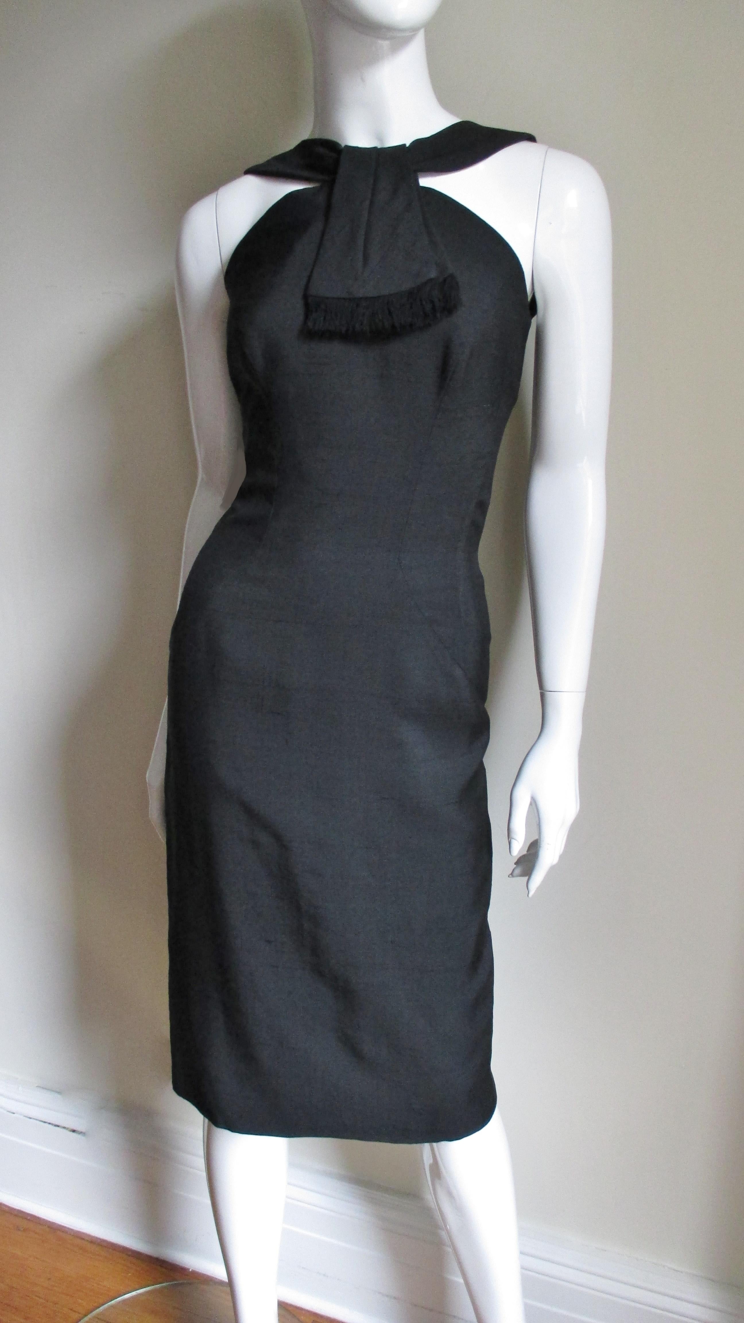 A stunning black silk dress from Estevez.  The neckline has 2 fringe edged overlapping panels at the center front and the back is low cut.  Intricate seaming creates a clever figure enhancing fit with princess seaming and curved insets at the waist.