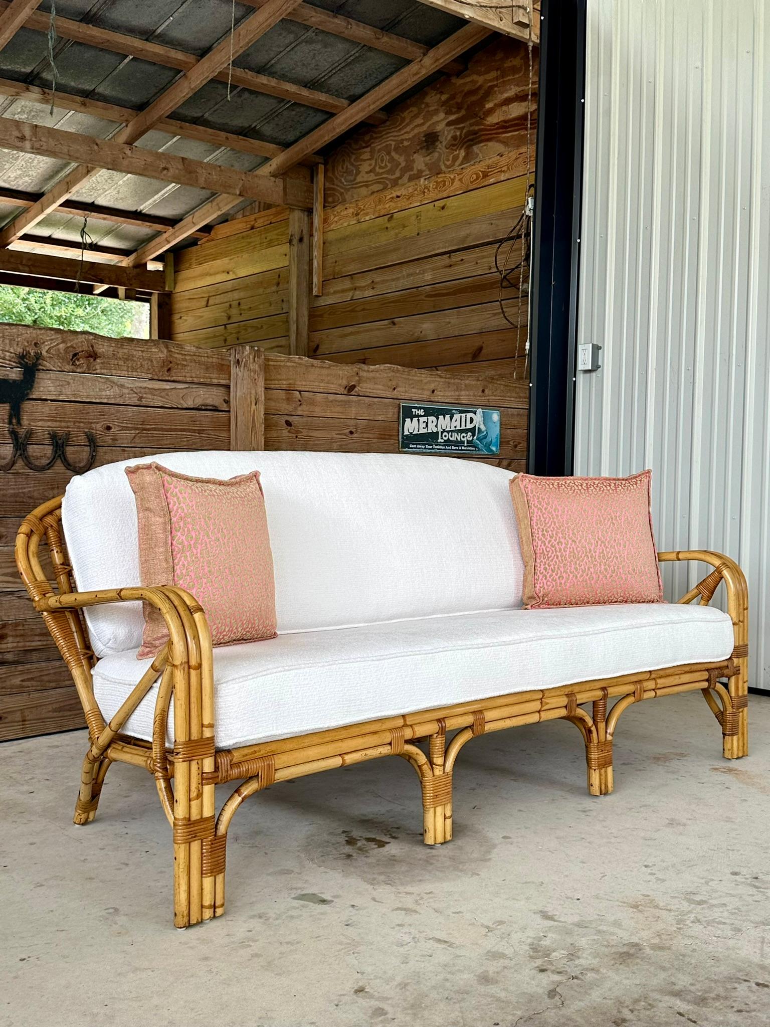 Exceptional vintage bent stick rattan refinished sofa that has new custom textured Boucle style white fabric and pink and green cheetah throw pillows.  Custom form fitted new cushions for a comfy cozy style with new textured white sunbrella fabric