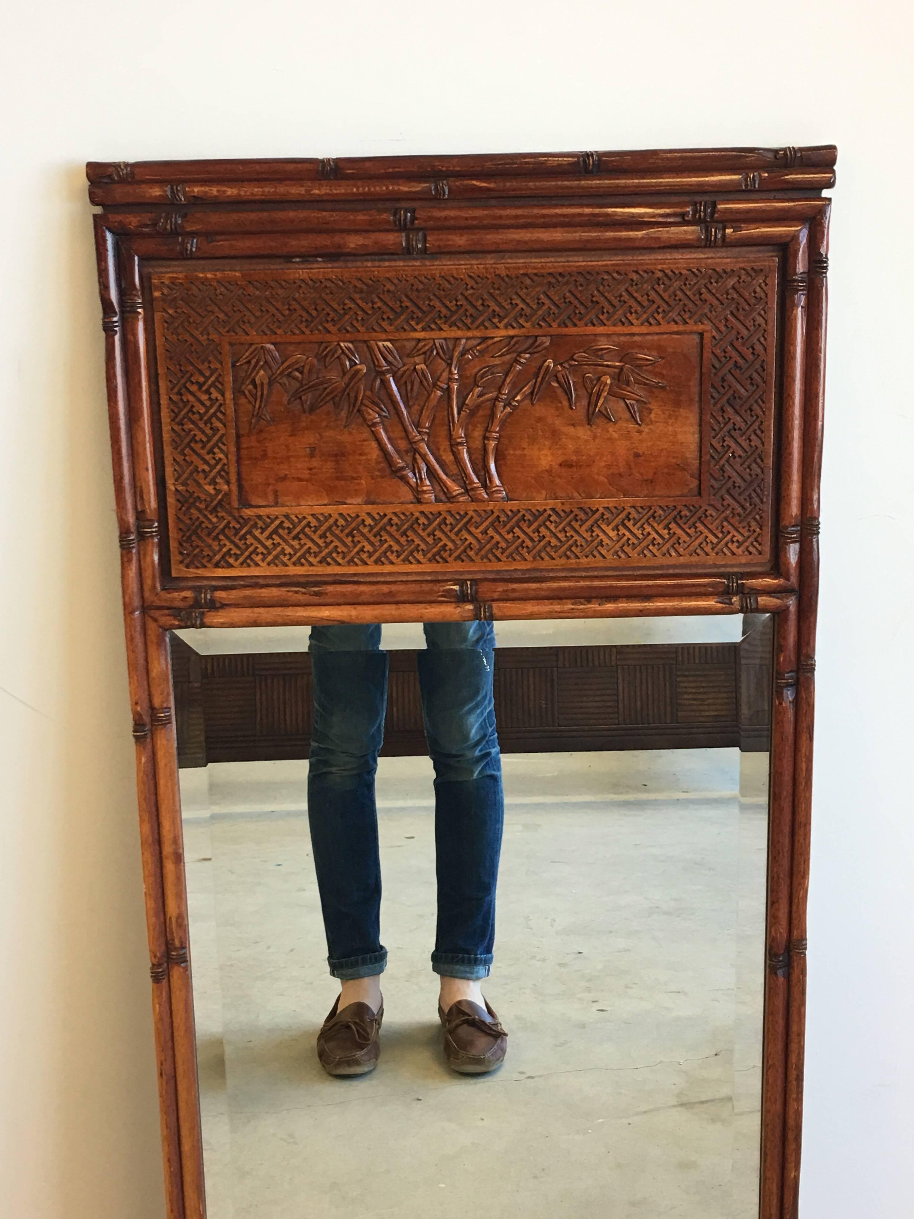 Offered is a beautiful, 1950s faux bamboo mirror. The piece features a faux bamboo border all around, with a Chinoiserie and Greek key detailed trumeau along the top. Beveled mirror.